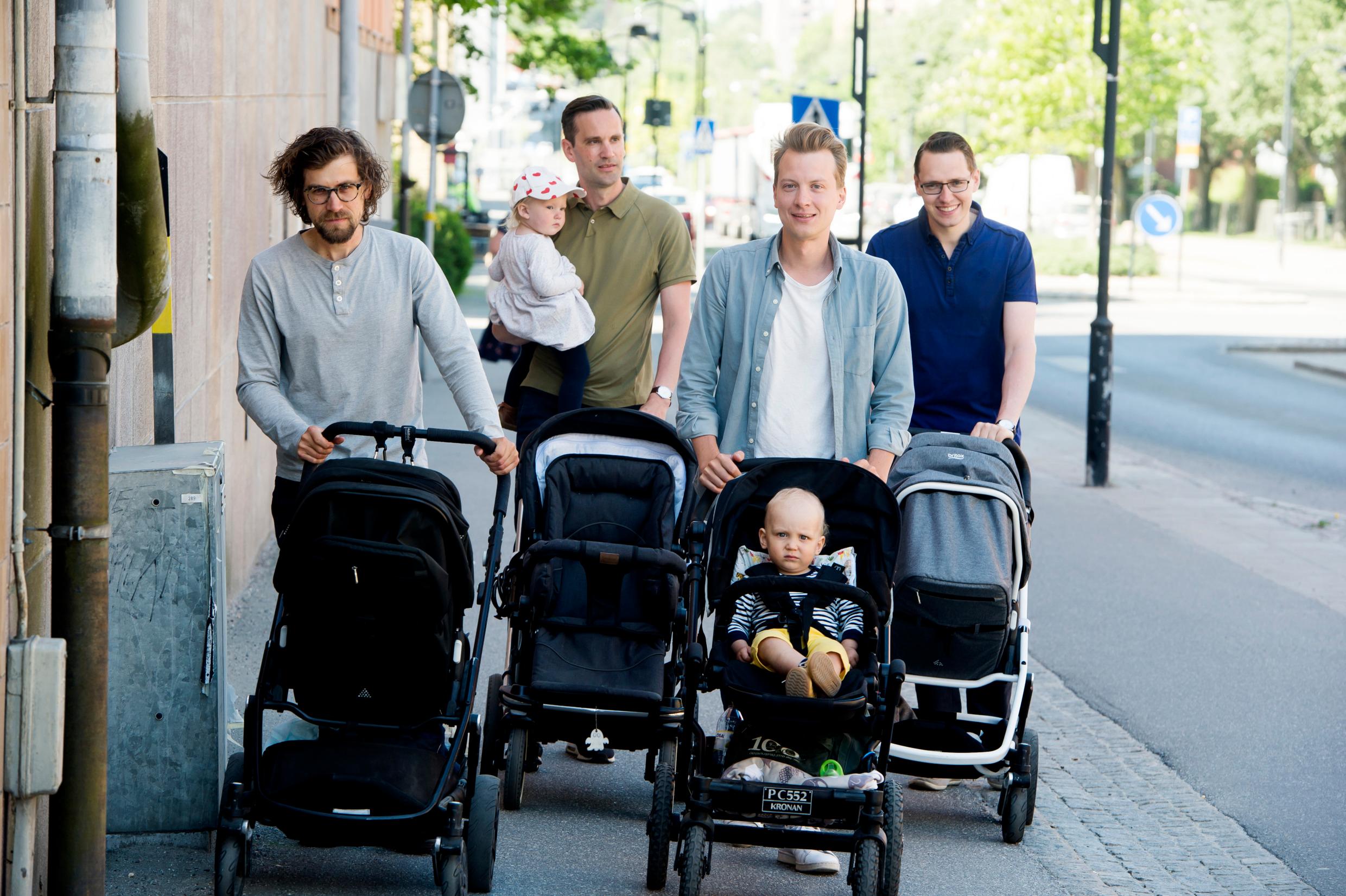 Four men with baby strollers walk down the street. Each man has a baby stroller.