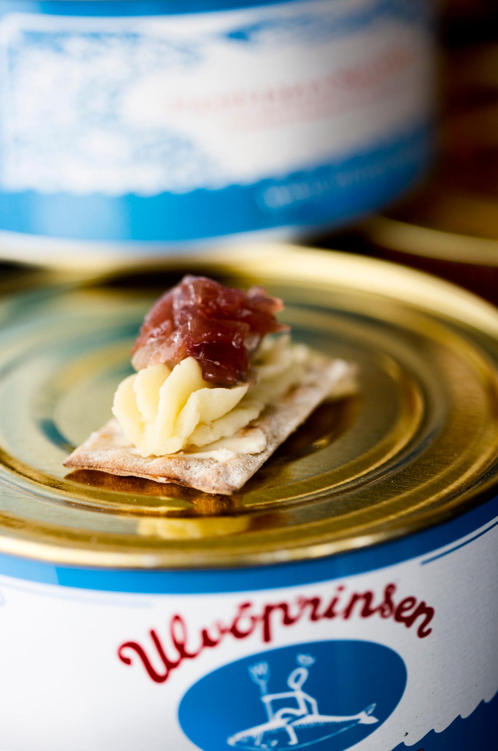 Tins of fermented herring. A tiny crispbread lies on top with some mashed potato and herring on.
