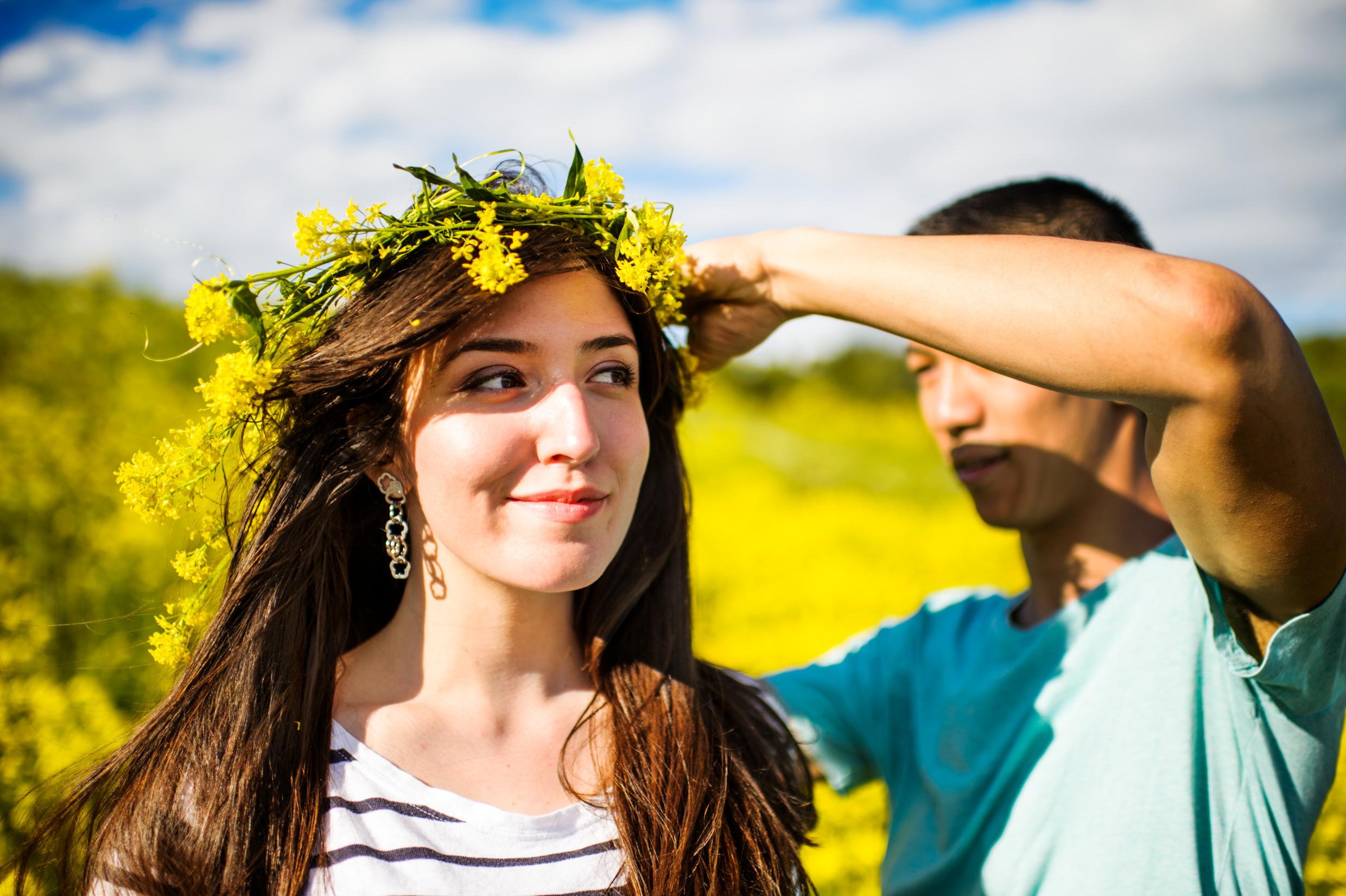 A man fitting a wreath of yellow flowers on a woman's head.
