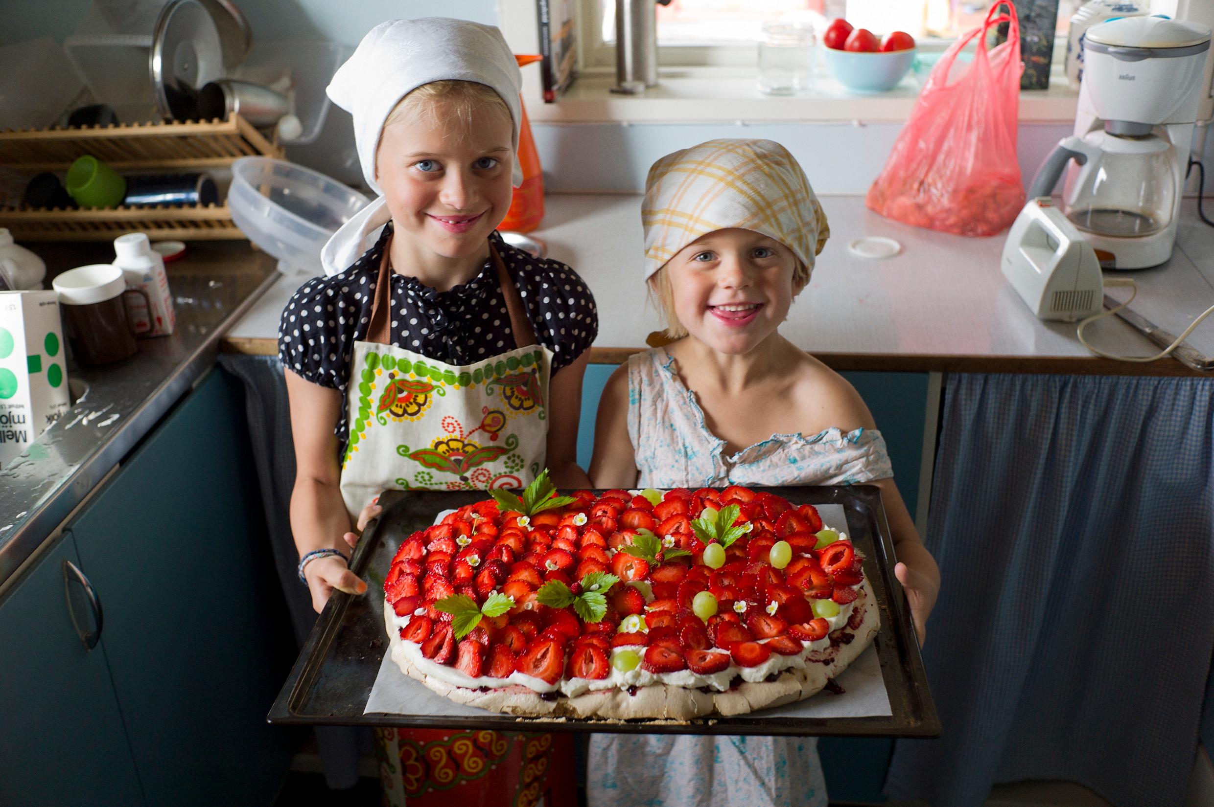 Two girls with headscarves and aprons holding a strawberry cake – one of many classic Swedish recipes.