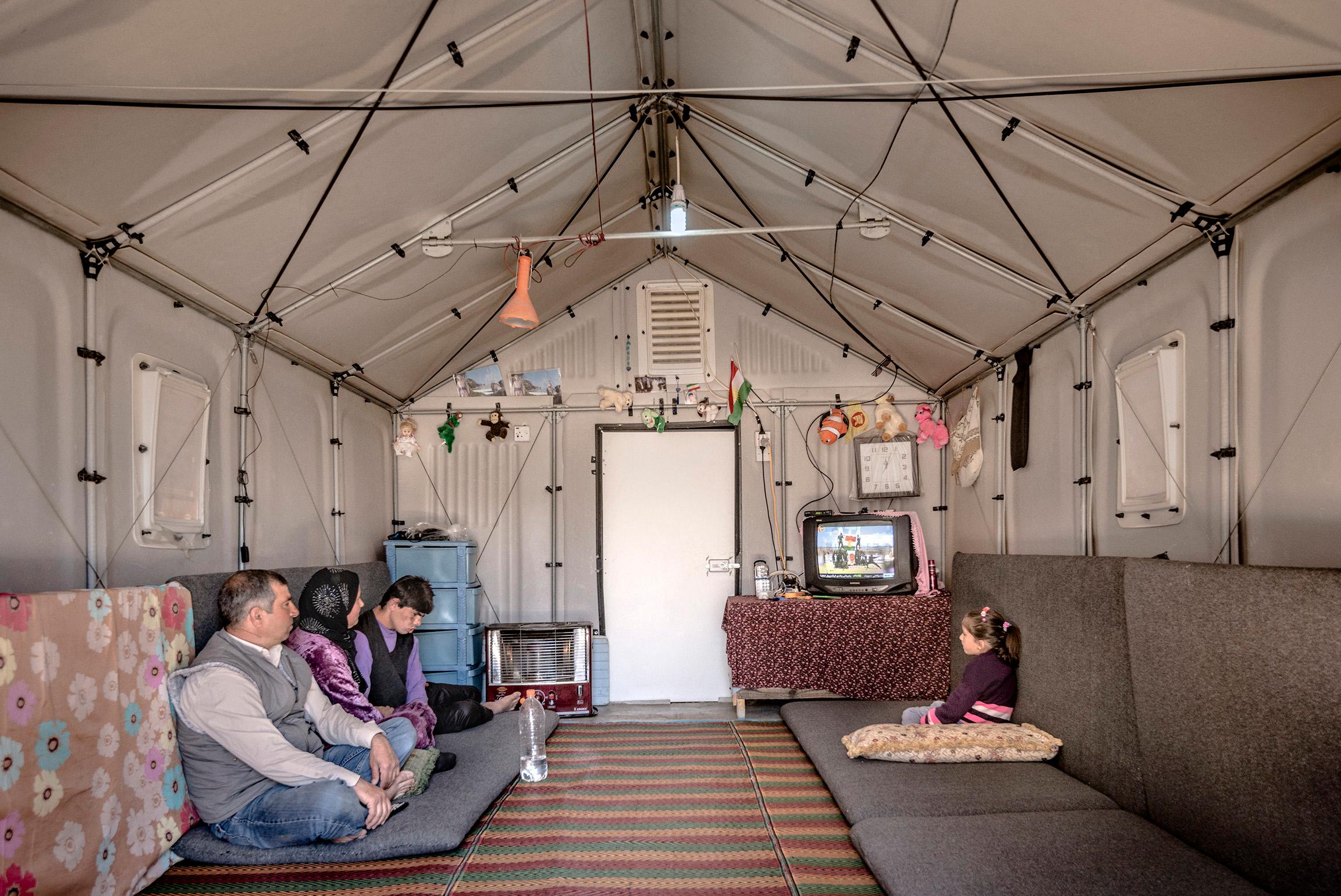 Two grown-ups and two children sitting on cushions on the floor in a tent with solid walls.