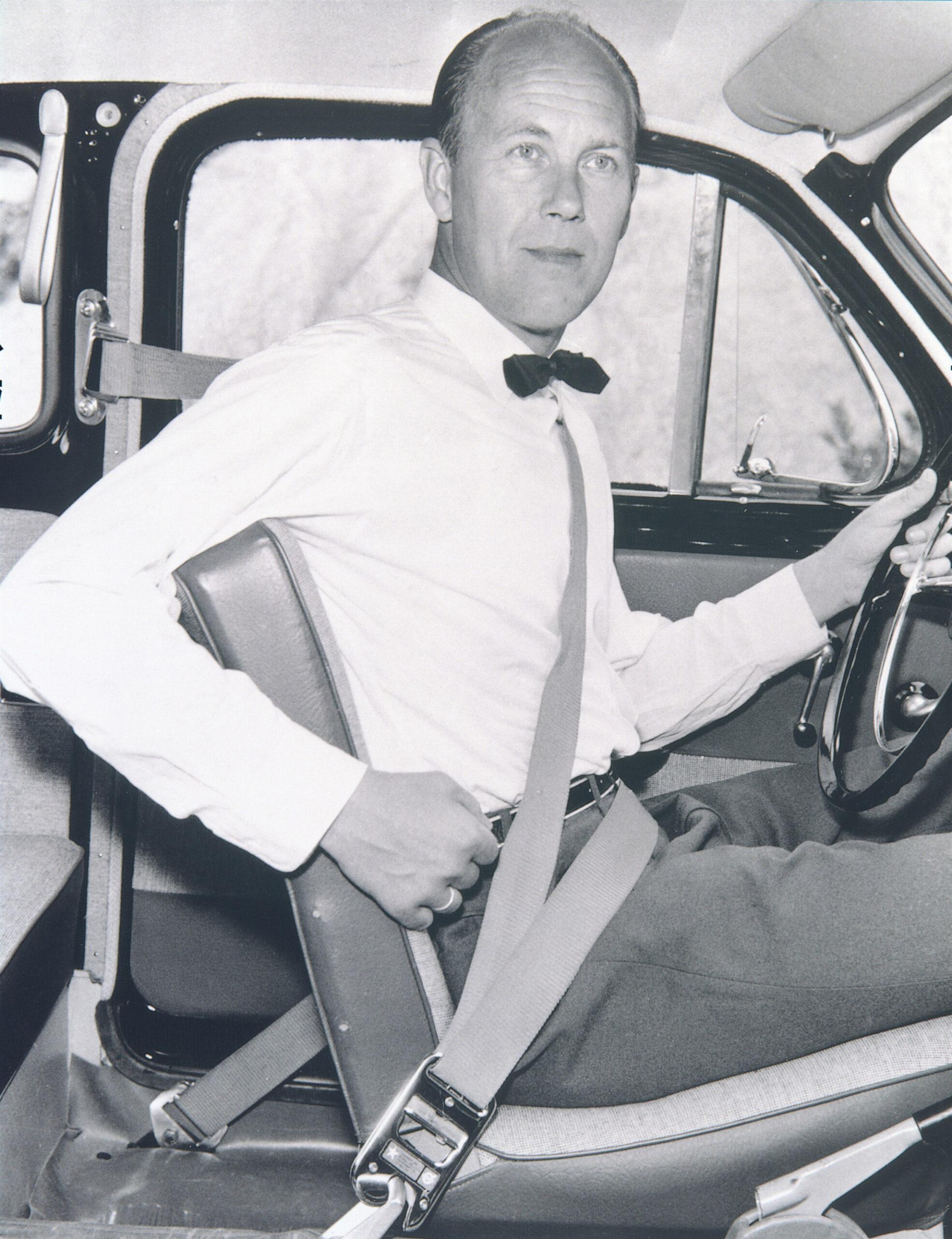 A black-and-white photo of a man in a car wearing a seatbelt.