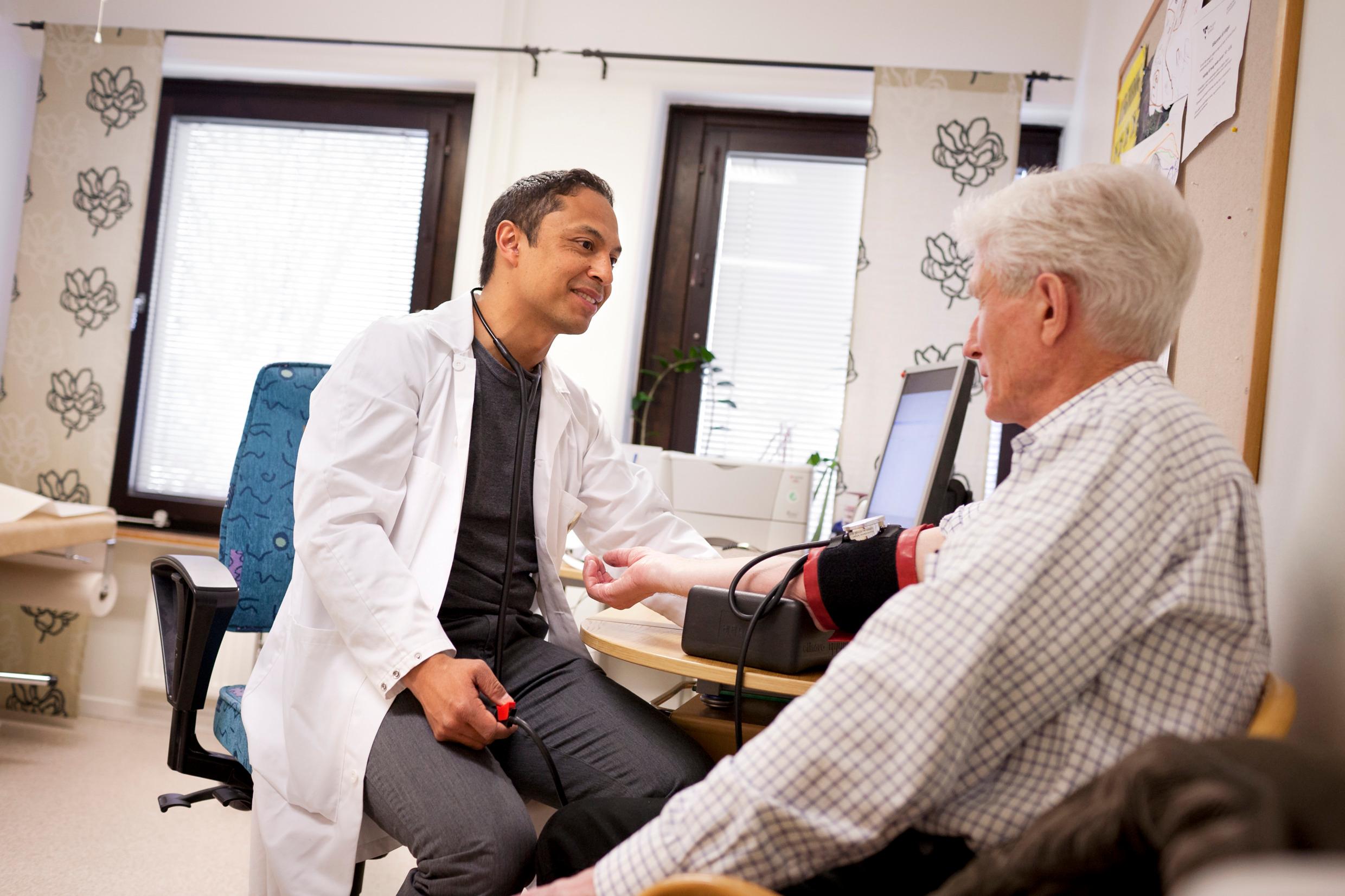 A doctor examining an older man, both sitting down, in a doctor's surgery.