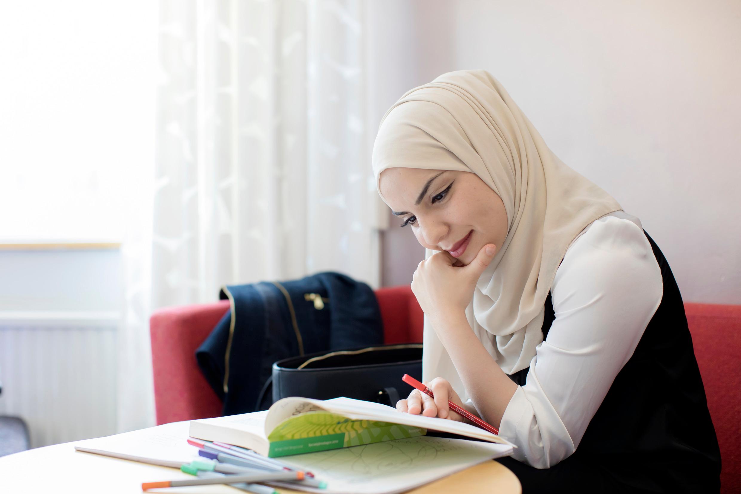 A woman wearing a veil sitting on a sofa reading something on a table in front of her.