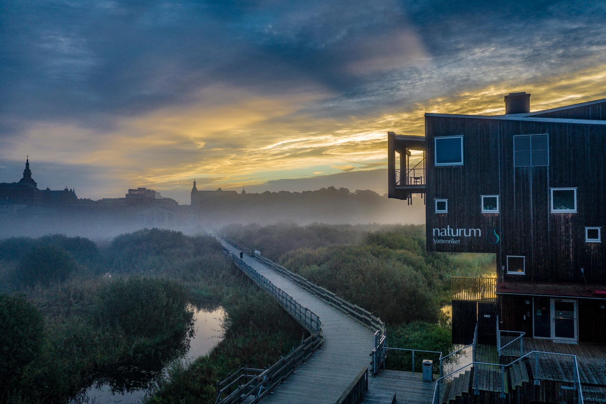 A dramatic twilight sky over a long walking path leading from a wooden building.