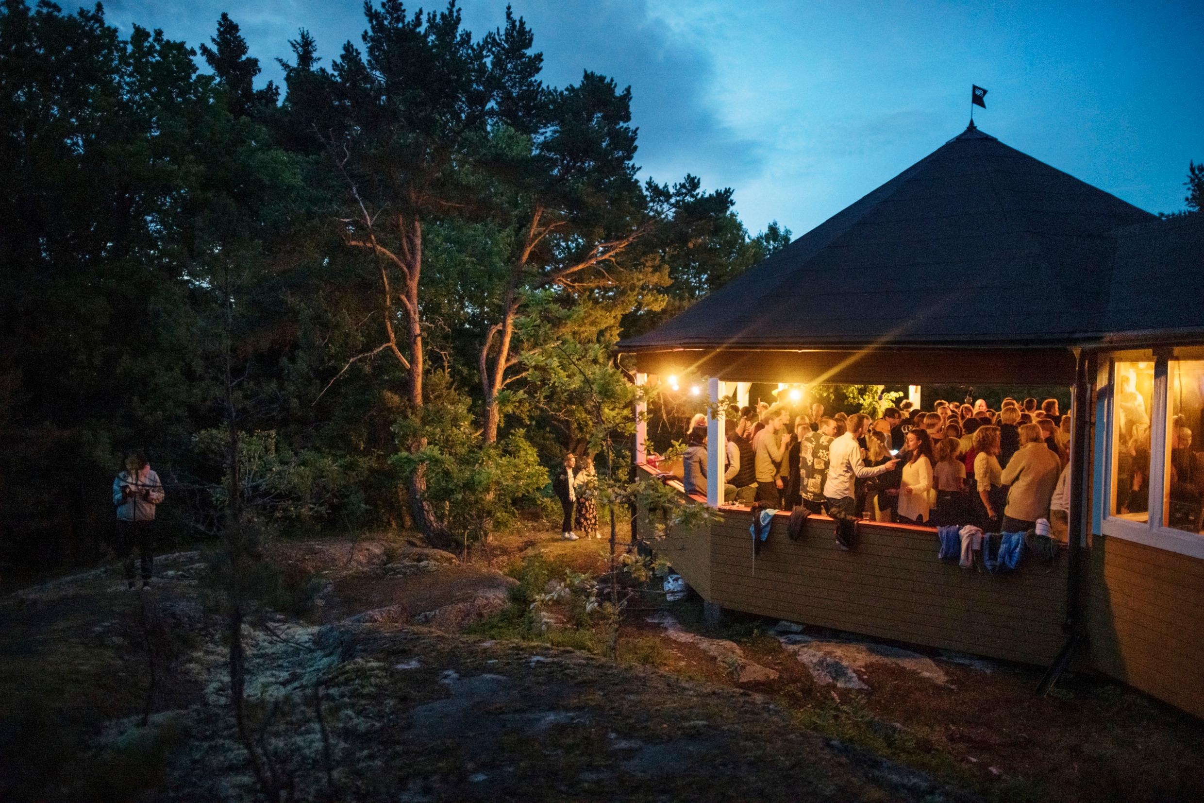 A roofed terrace is full of people. It's dark and the terrace is lit.