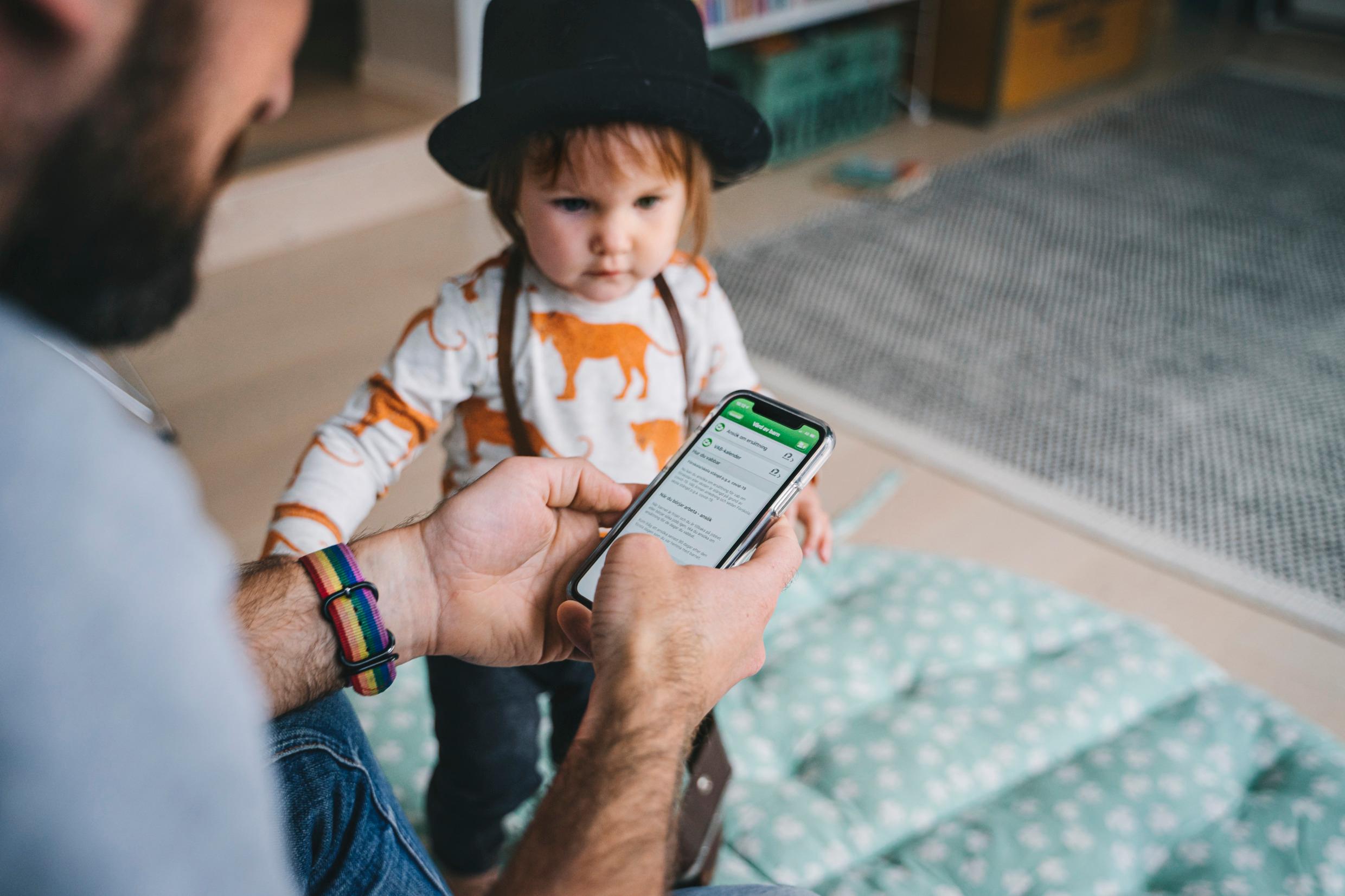 A man is using his phone while his child watches.