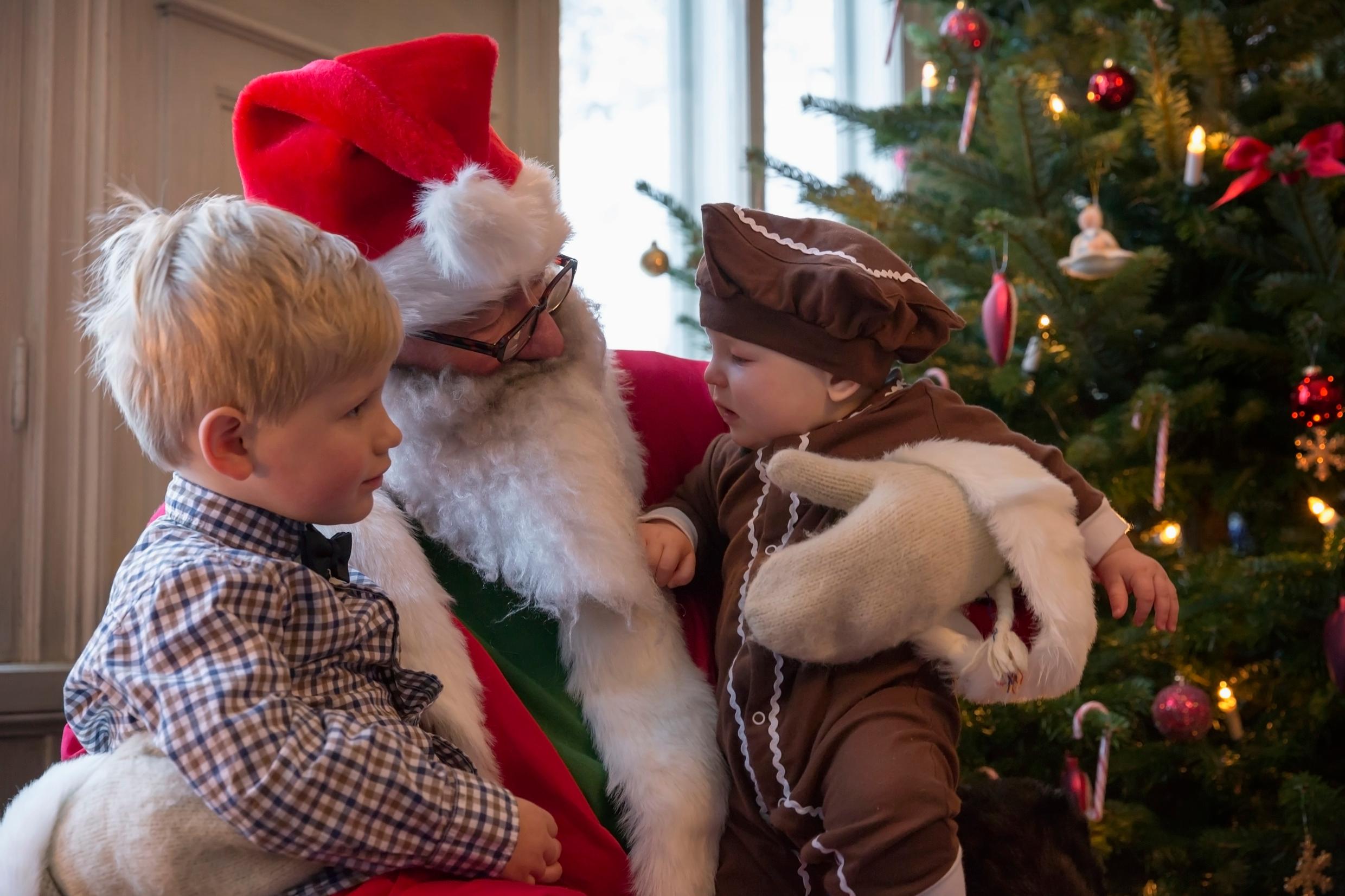 A man dressed up as Father Christmas, with a child on each knee. A Christmas tree in the background.