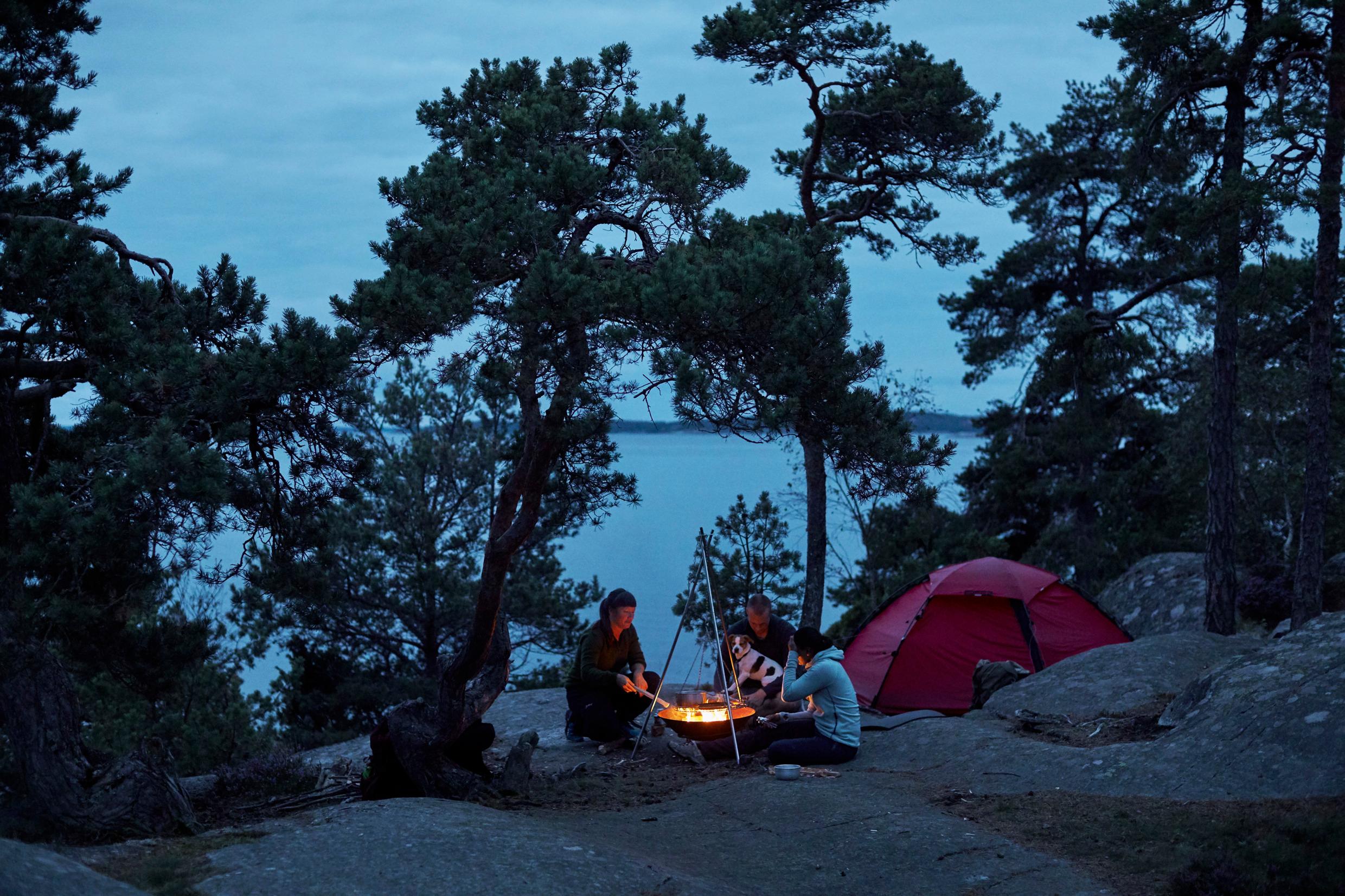 Three people around a camp fire at night, a tent in the background.