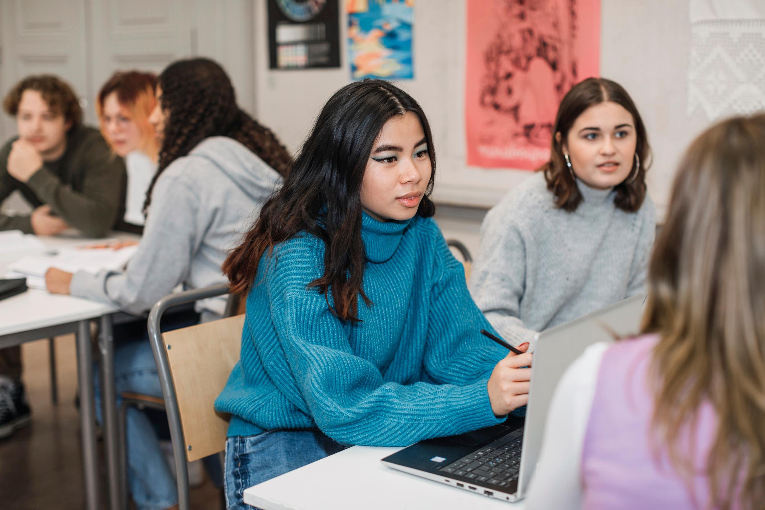 Students sit around desks with their laptops and books.