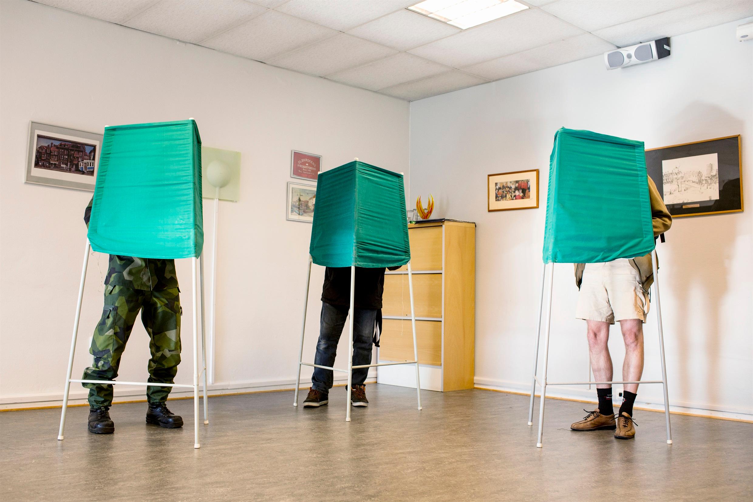 A polling station, where all we can see is three people's legs beneth green screens.