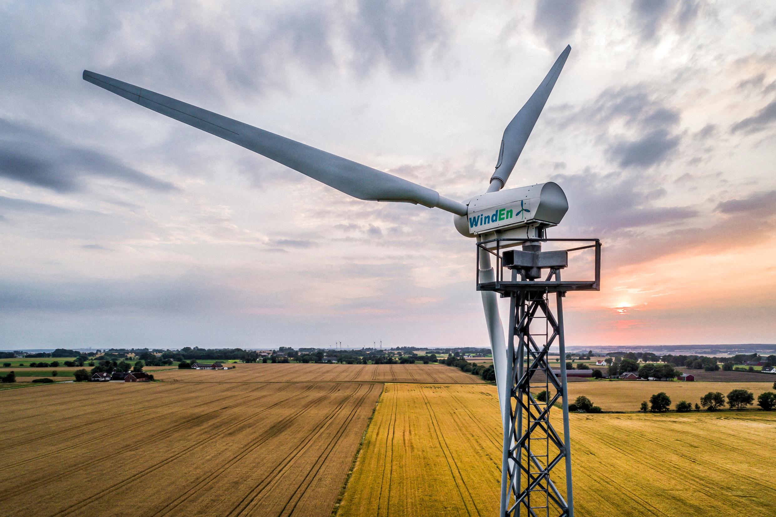 A wind turbine in the foreground, yellow fields and a sunset in the background.