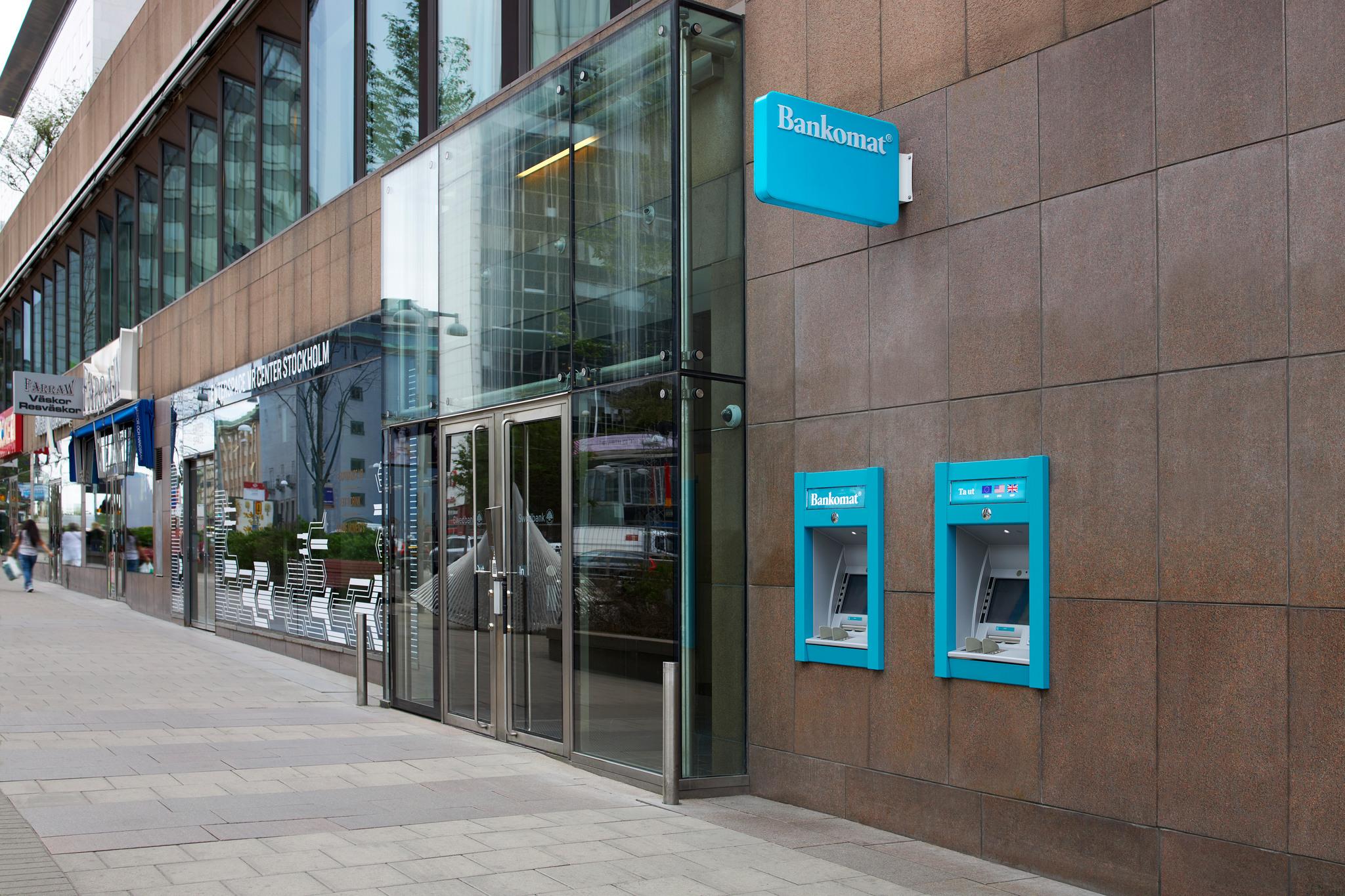 A cash machine in a wall by an empty street.