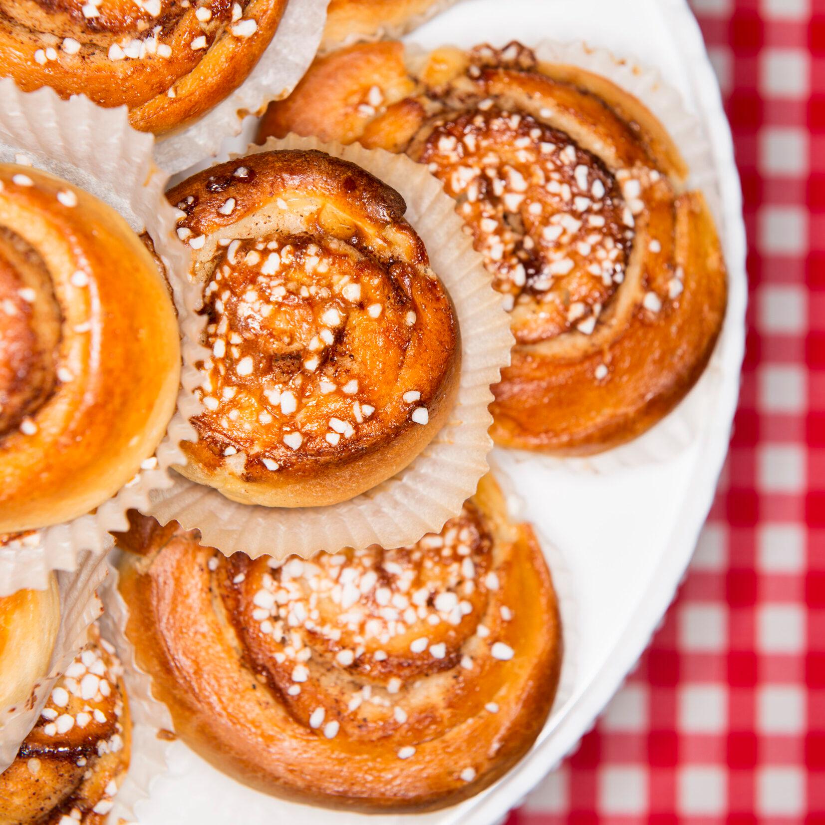 Seen from above, a plate filled with cinnamon buns on top of a red and white table cloth.