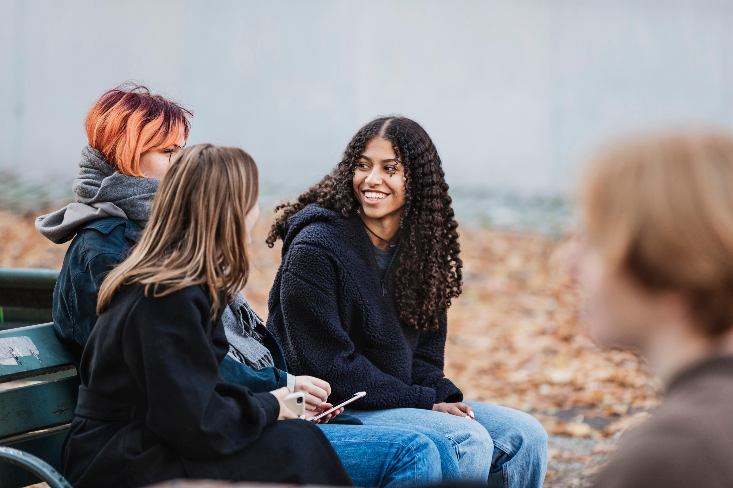 Three girls on a park bench. Someone passes by, blurred.