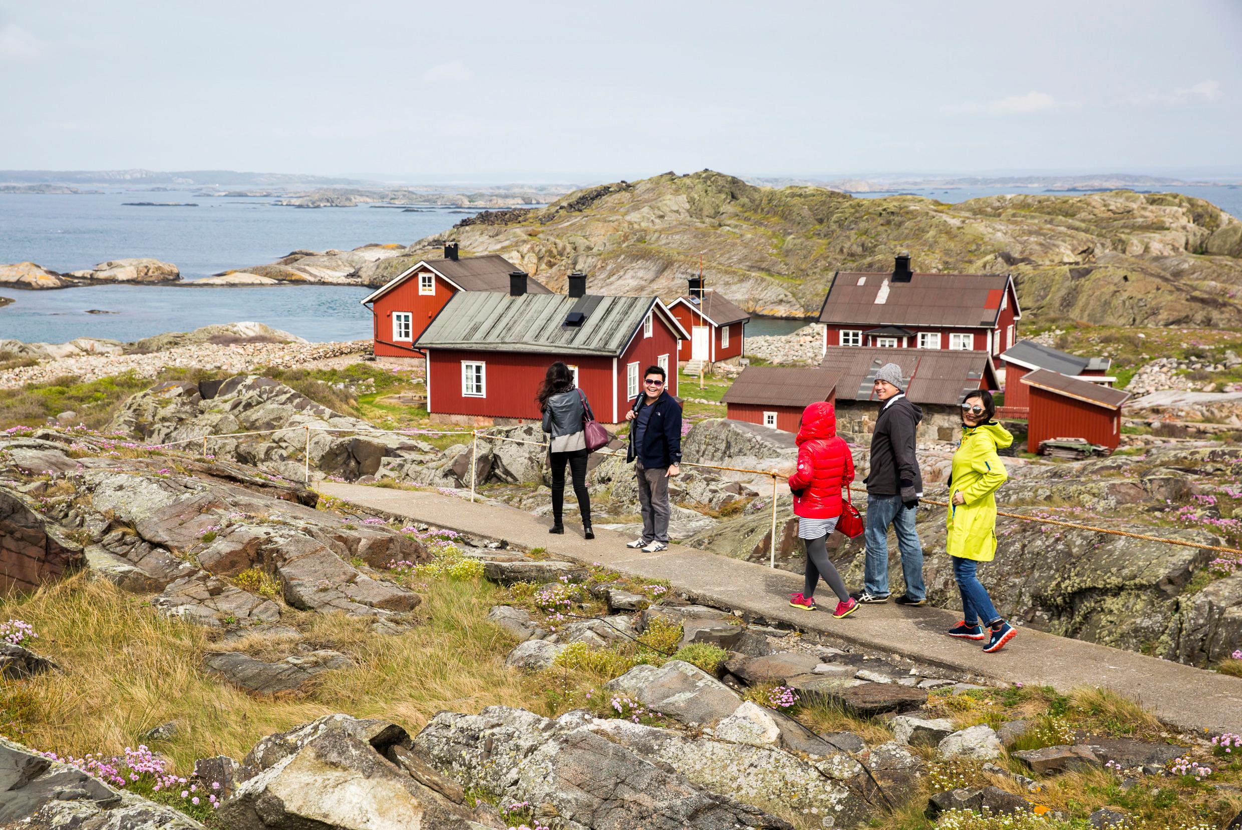 A group of people walk through the rocky island landscape of Kosterhavet National Park, passing a few small red houses.