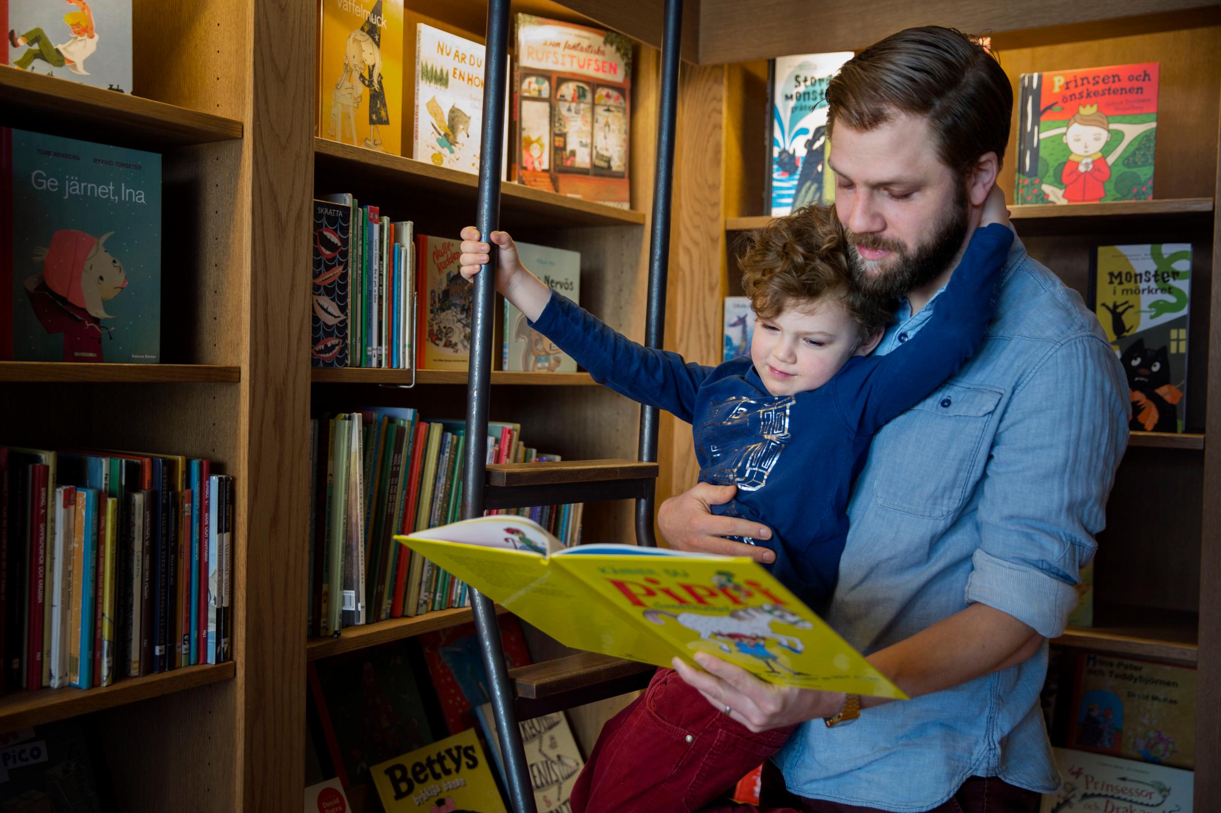 A son leaning against his father, who holds an open Pippi Longstocking book in his hand.