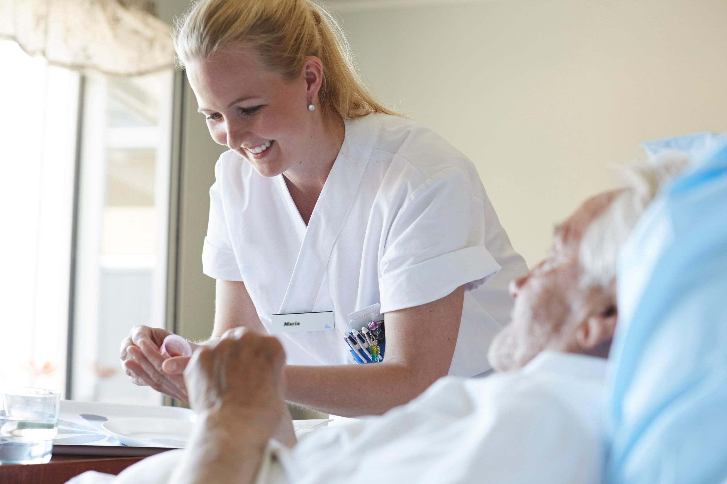 A nurse taking care of an older man lying in a hospital bed.