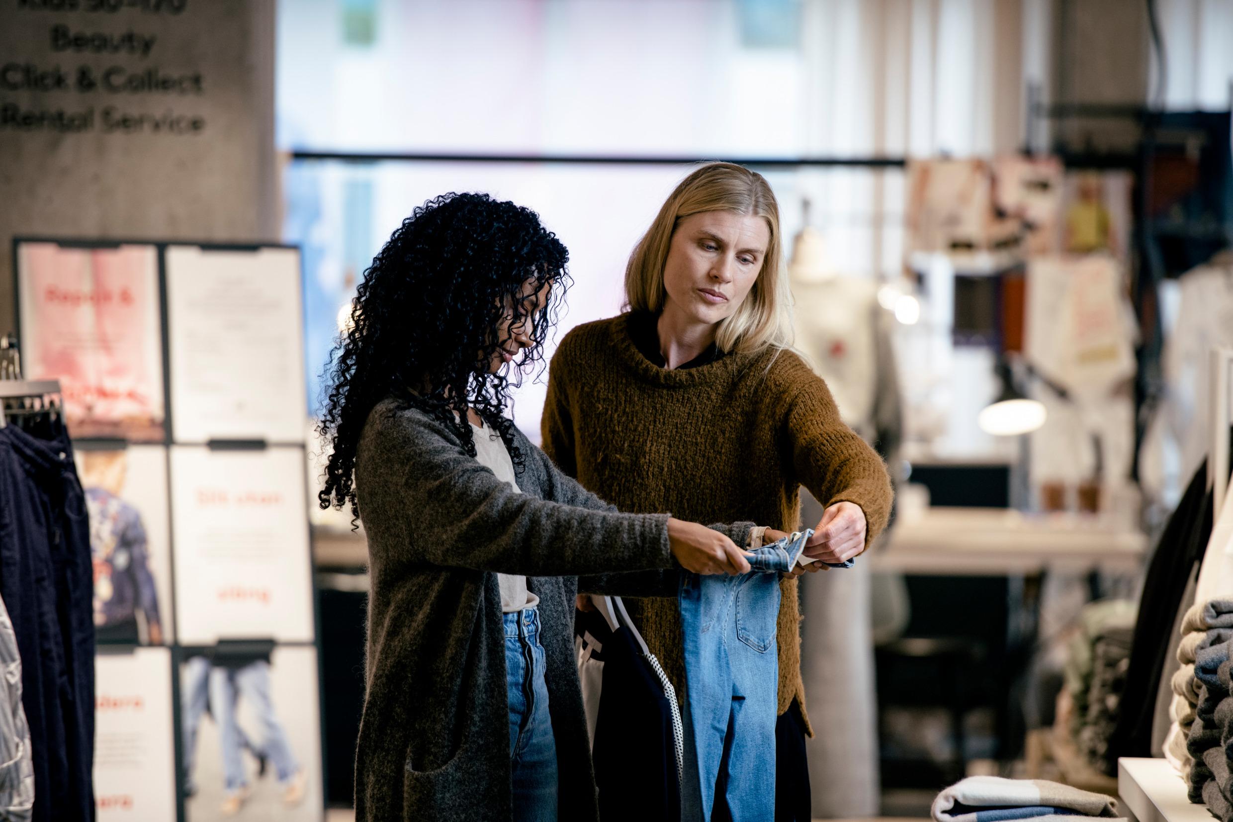 Two women in a clothes shop inspecting a pair of jeans.