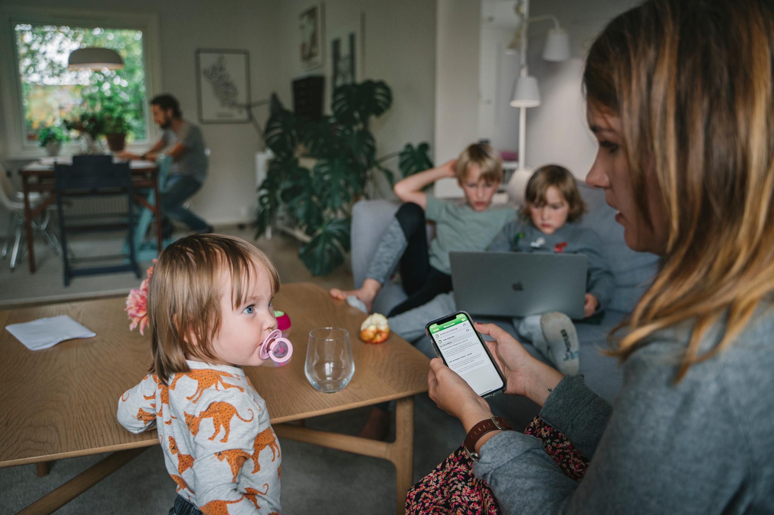 A mother on the sofa with three children, and a father in the background.