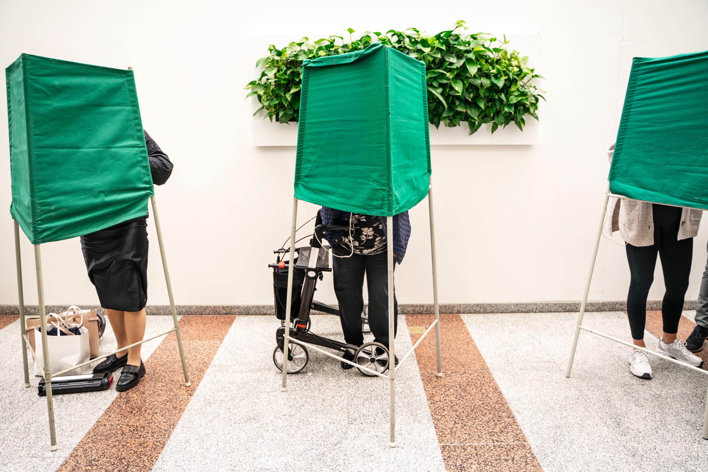 Three people stand behind green screens.