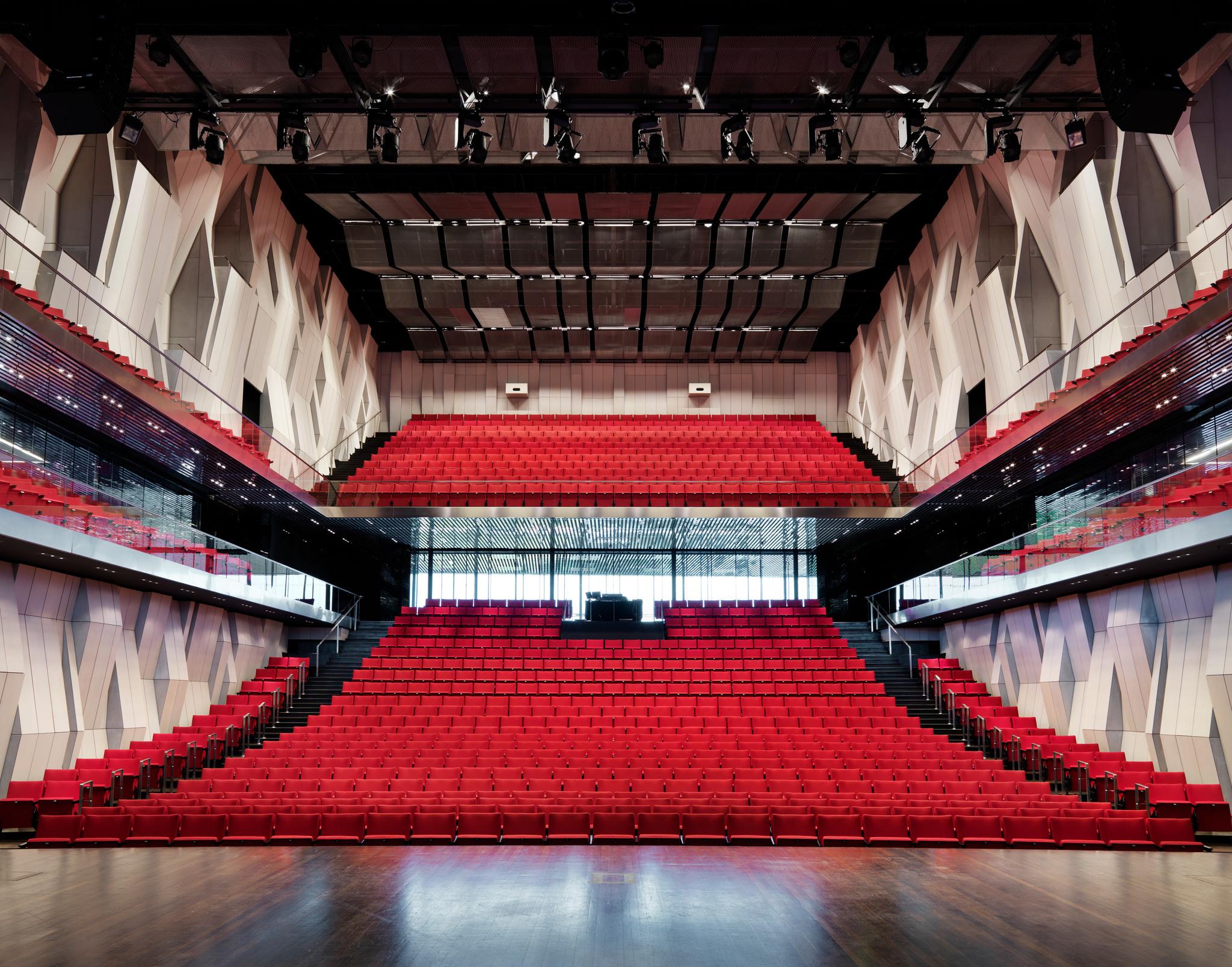 The interior of a concert hall, with red seats.