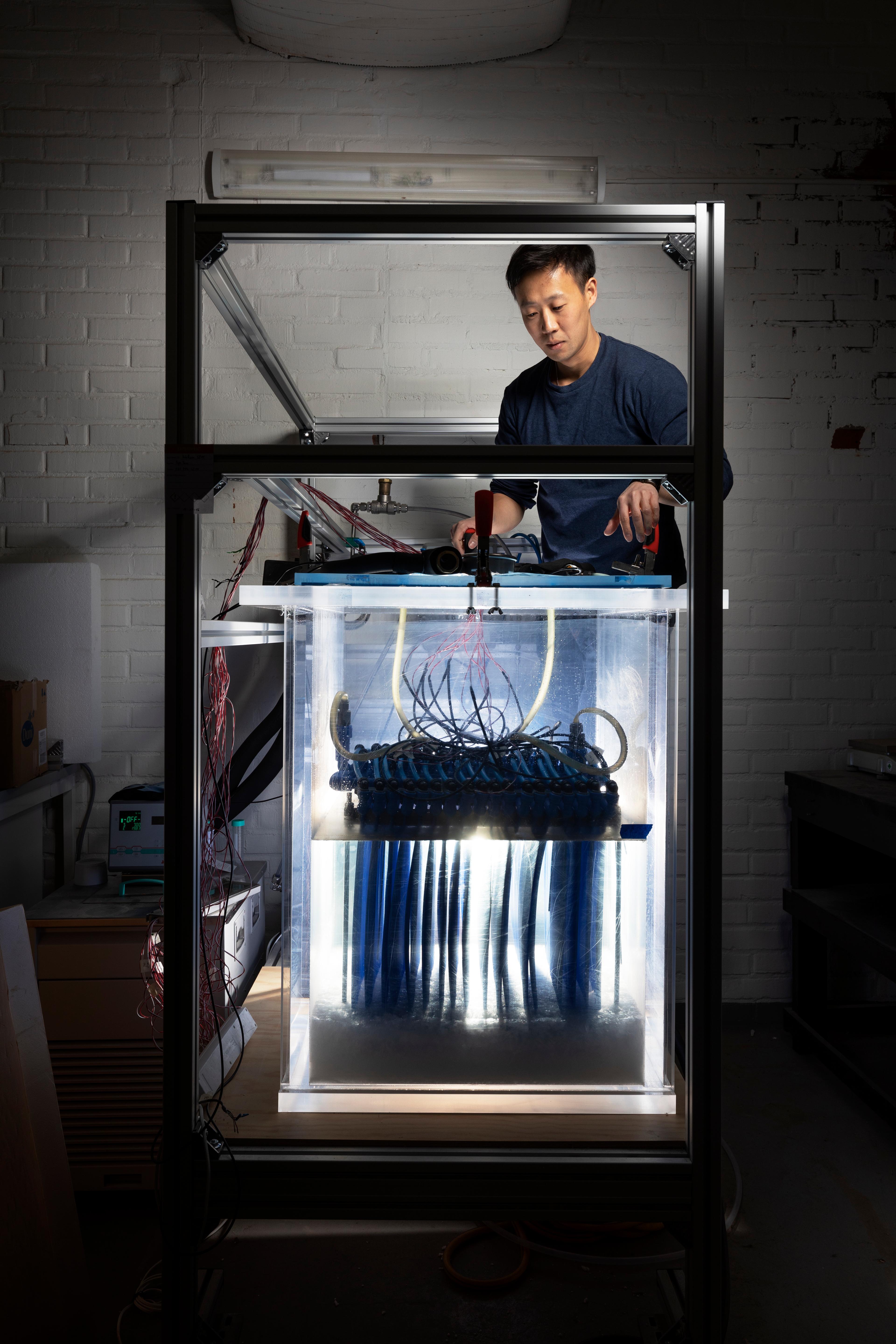 A man is standing above a glass container holding wires and a blue metal container.