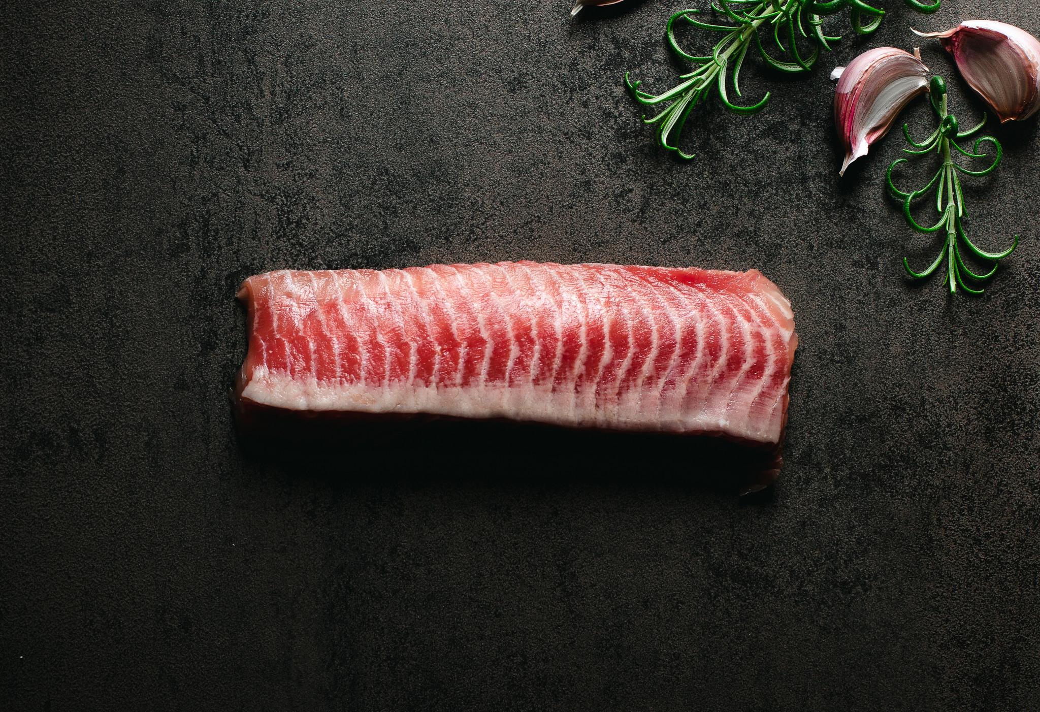 A red filleted fish on a black surface.