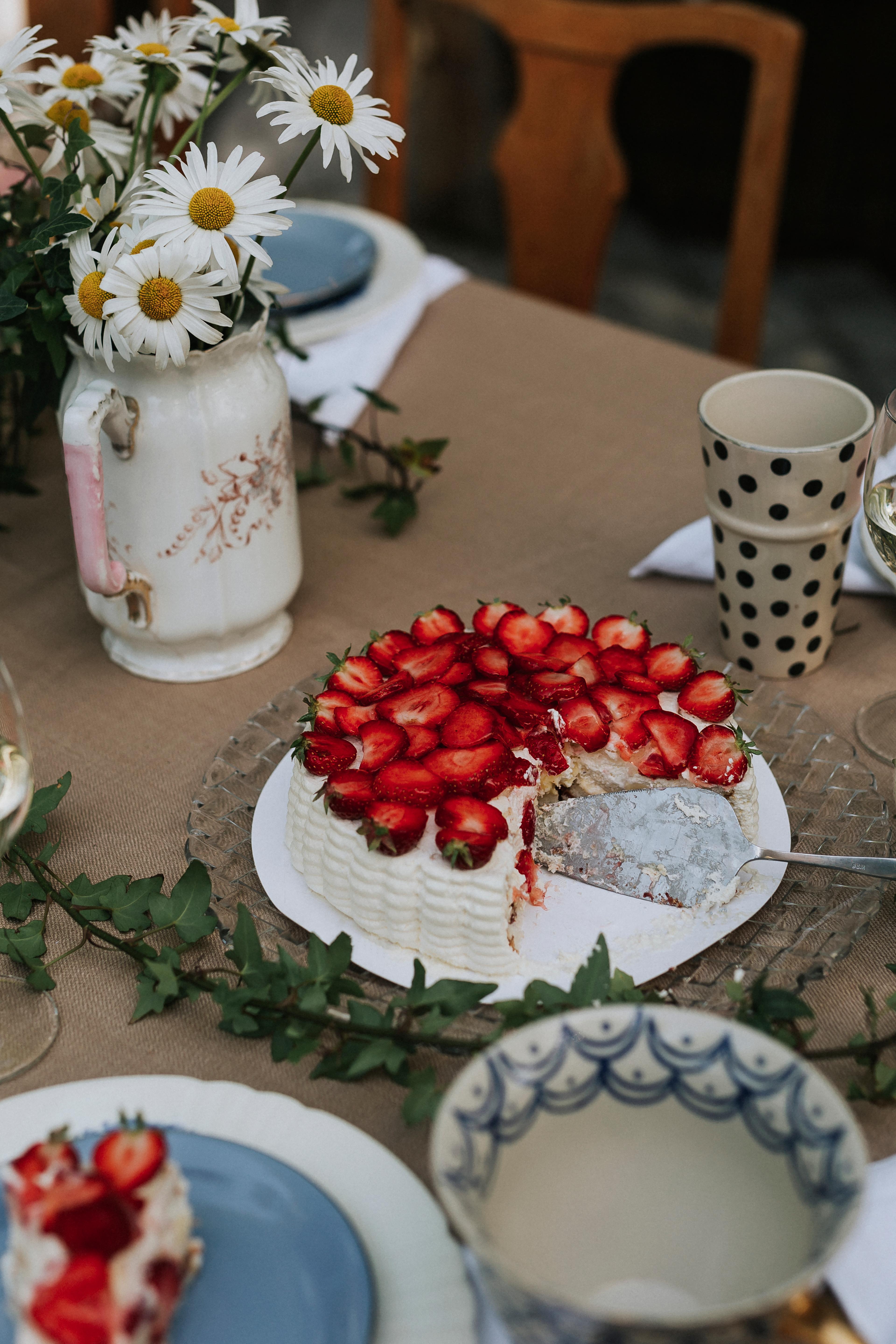 Strawberry cake on a set table with flowers and plates.