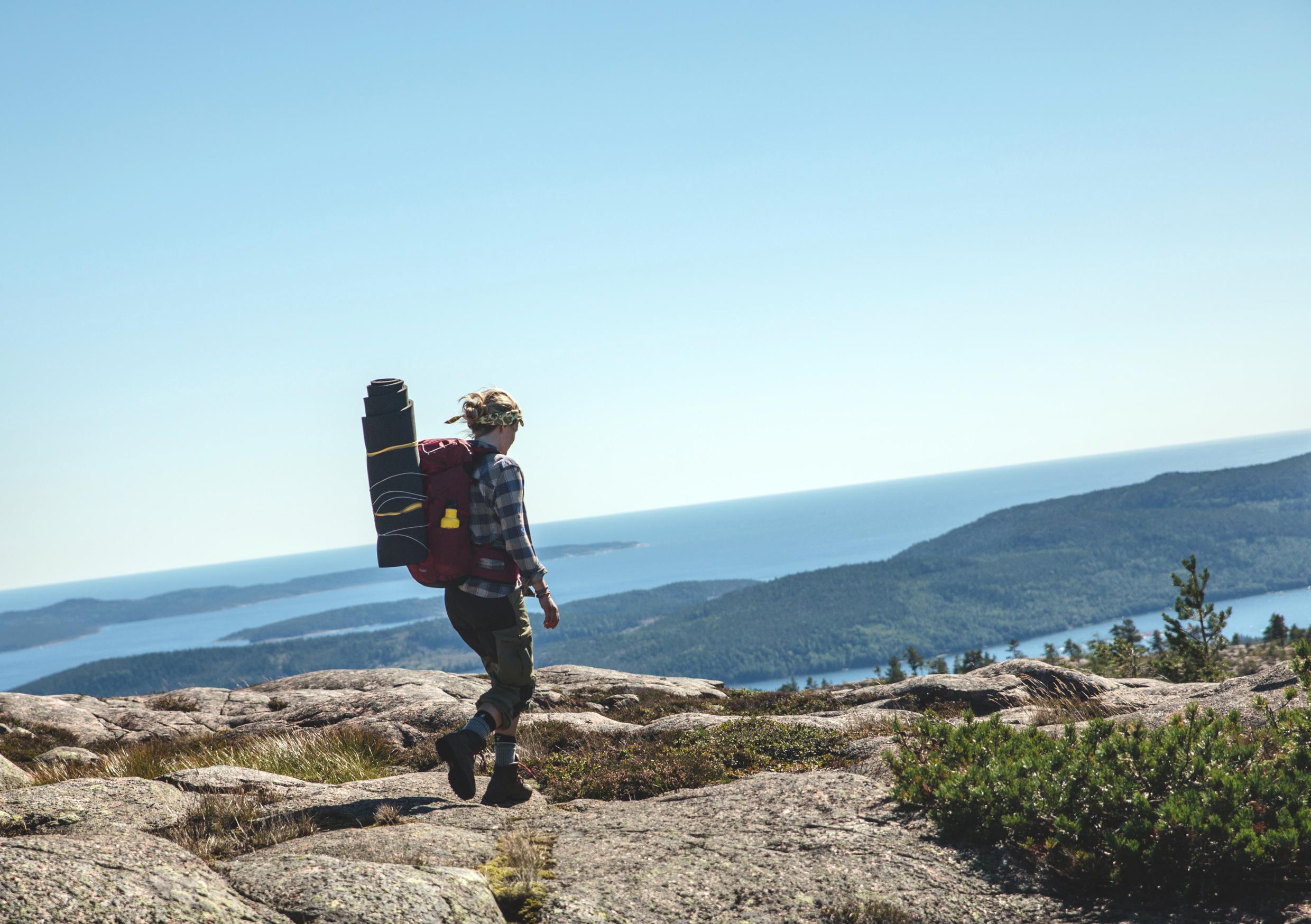 A woman with a backpack is hiking on one of the peaks of the Swedish High Coast overlooking the Baltic Sea.