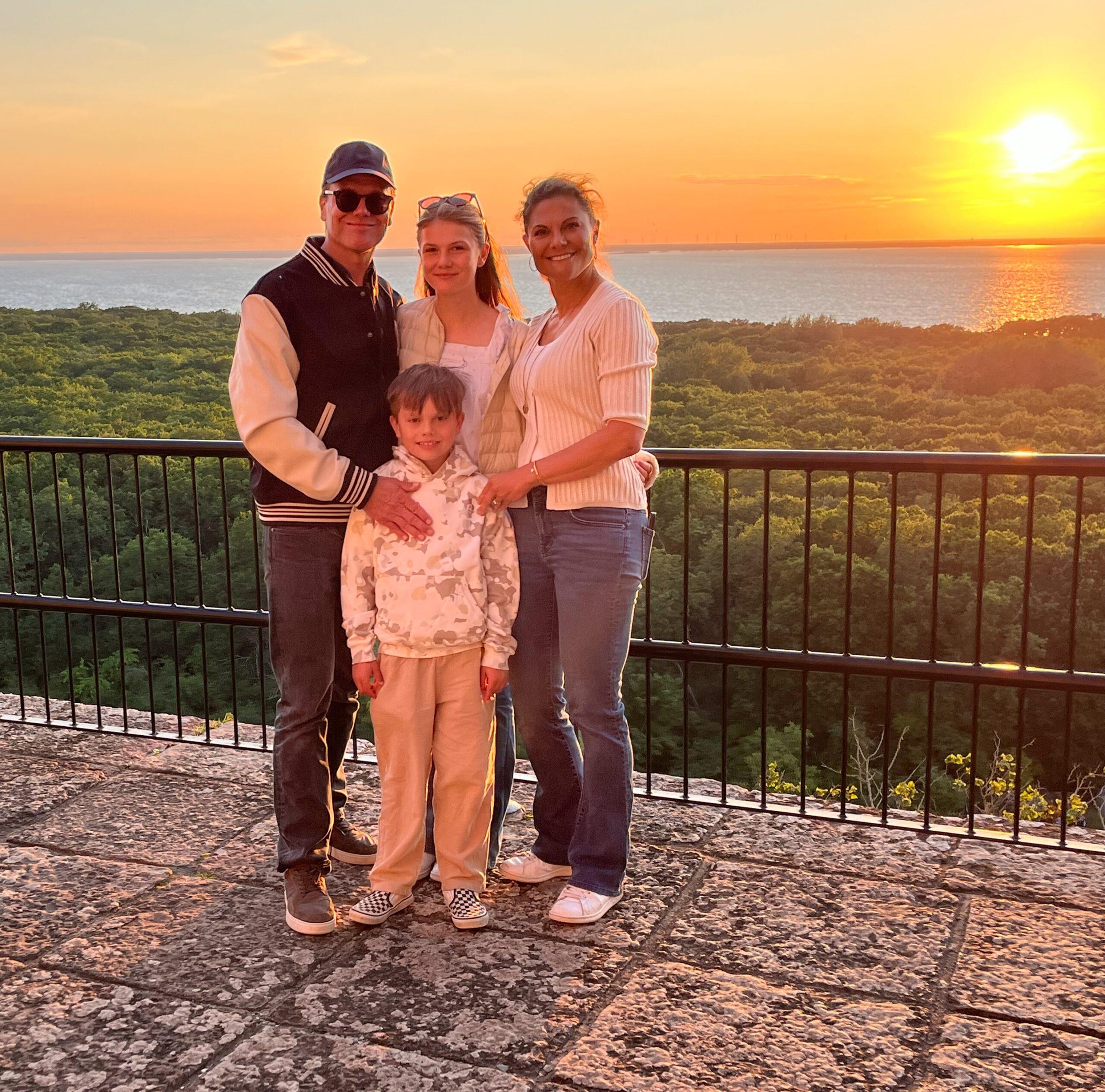 A father, a mother and two children standing close together - a sunset in the background.