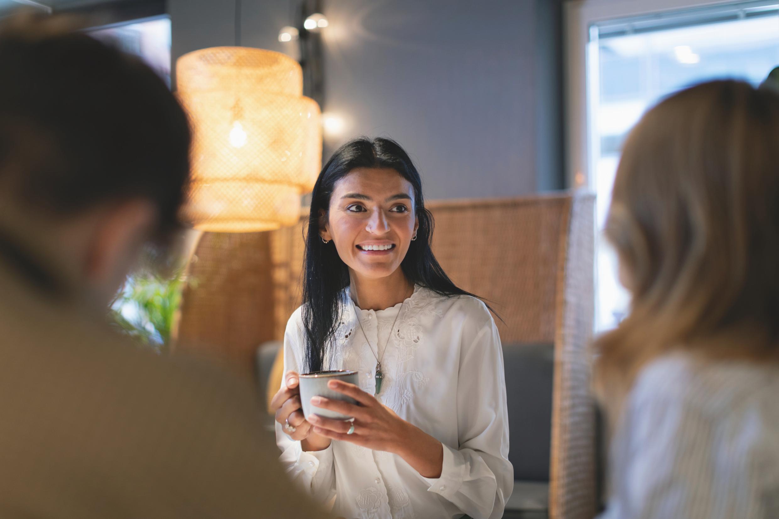 People sit around a table, holding coffee mugs.