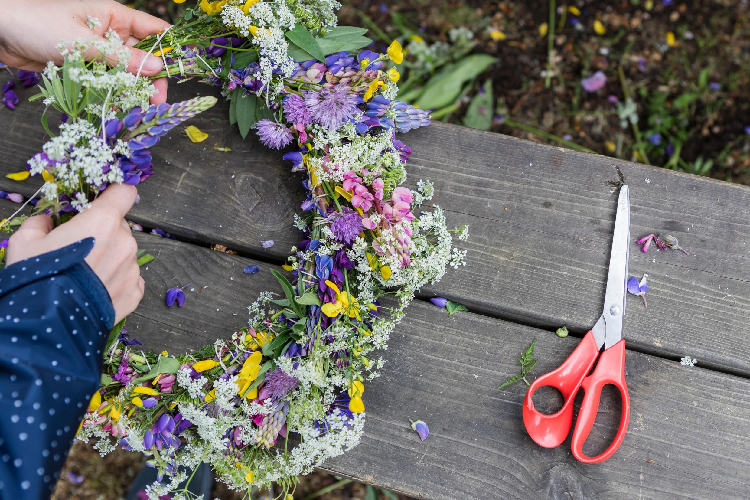 Two hands making a flower wreath. Scissors on the side.