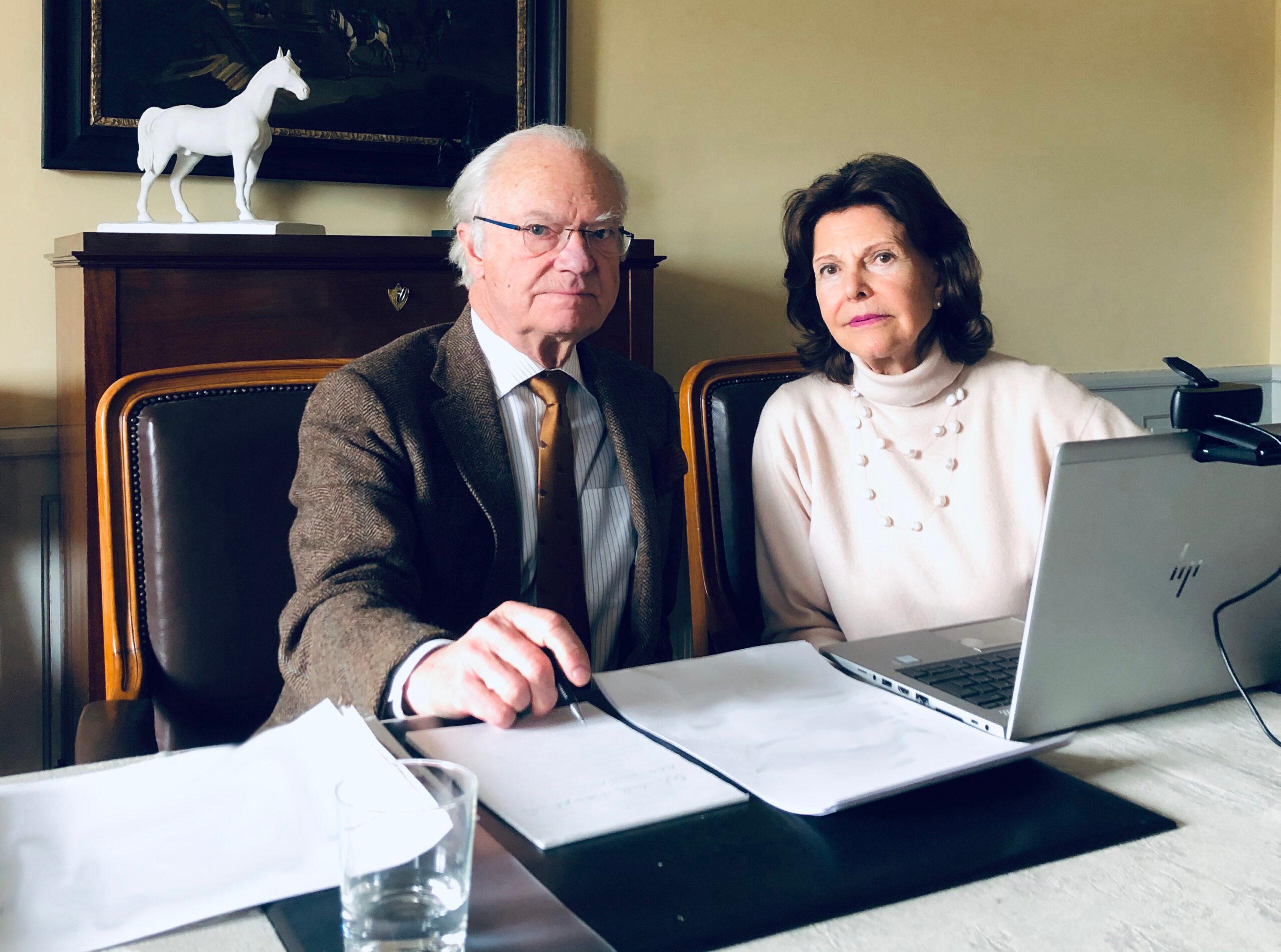 King Carl XVI Gustaf and Queen Silvia at a desk with a computer with a camera.