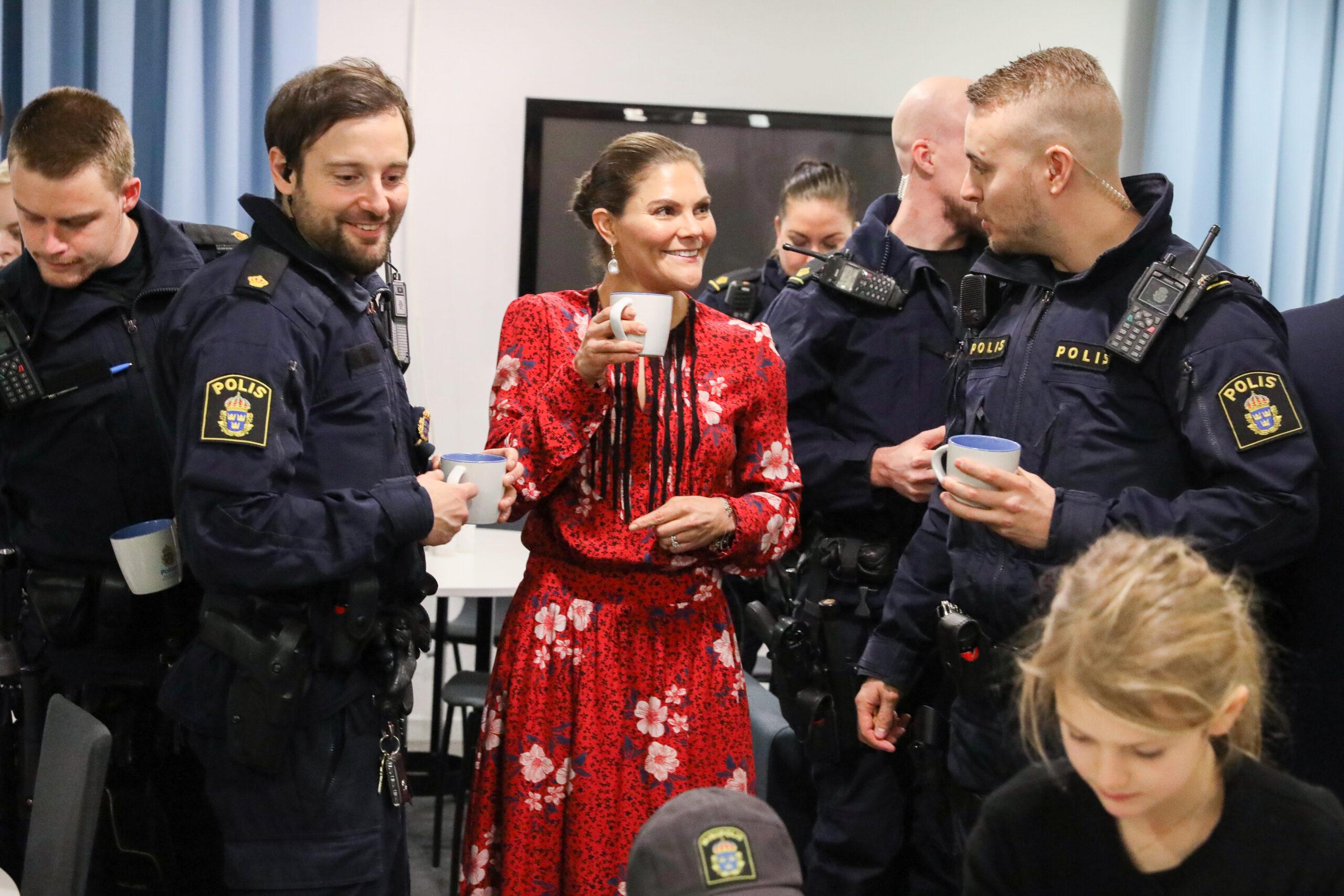 Crown Princess Victoria drinking coffee with police officers in uniform.