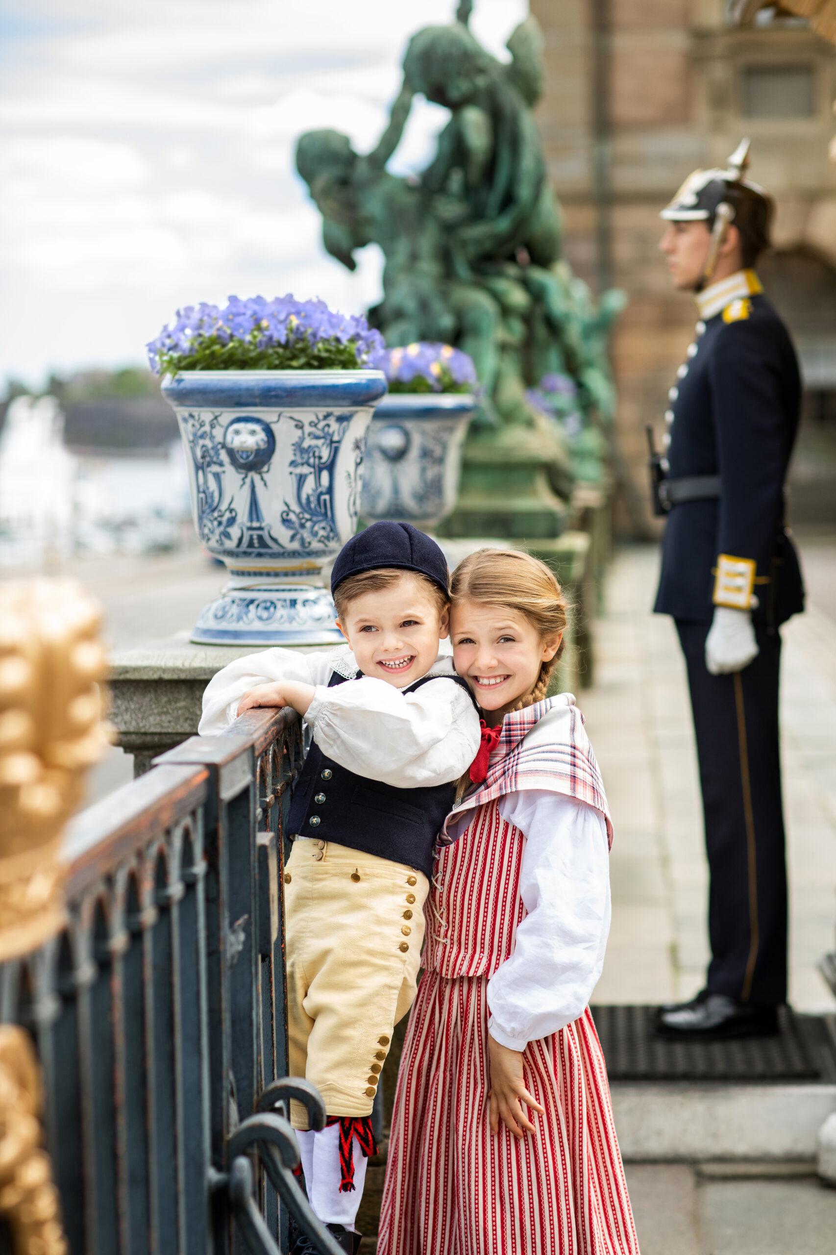 Princess Estelle and Prince Oscar dressed up and standing by a railing, a uniformed guard in the background.