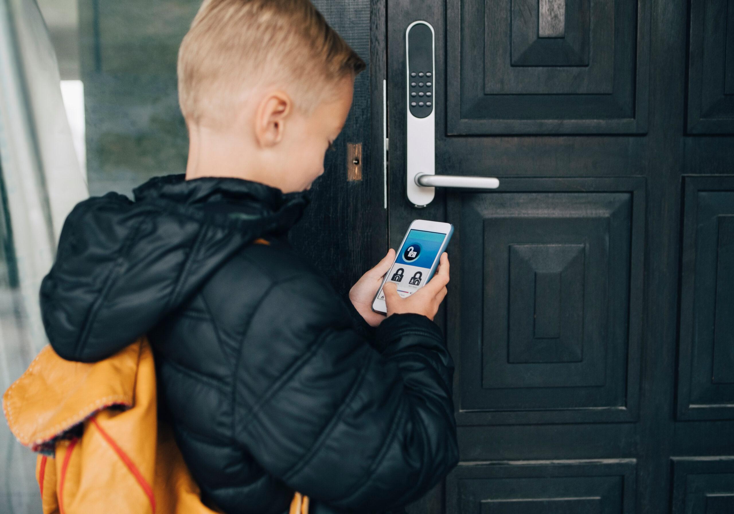 A boy standing with a mobile phone in his hand outside a front door.