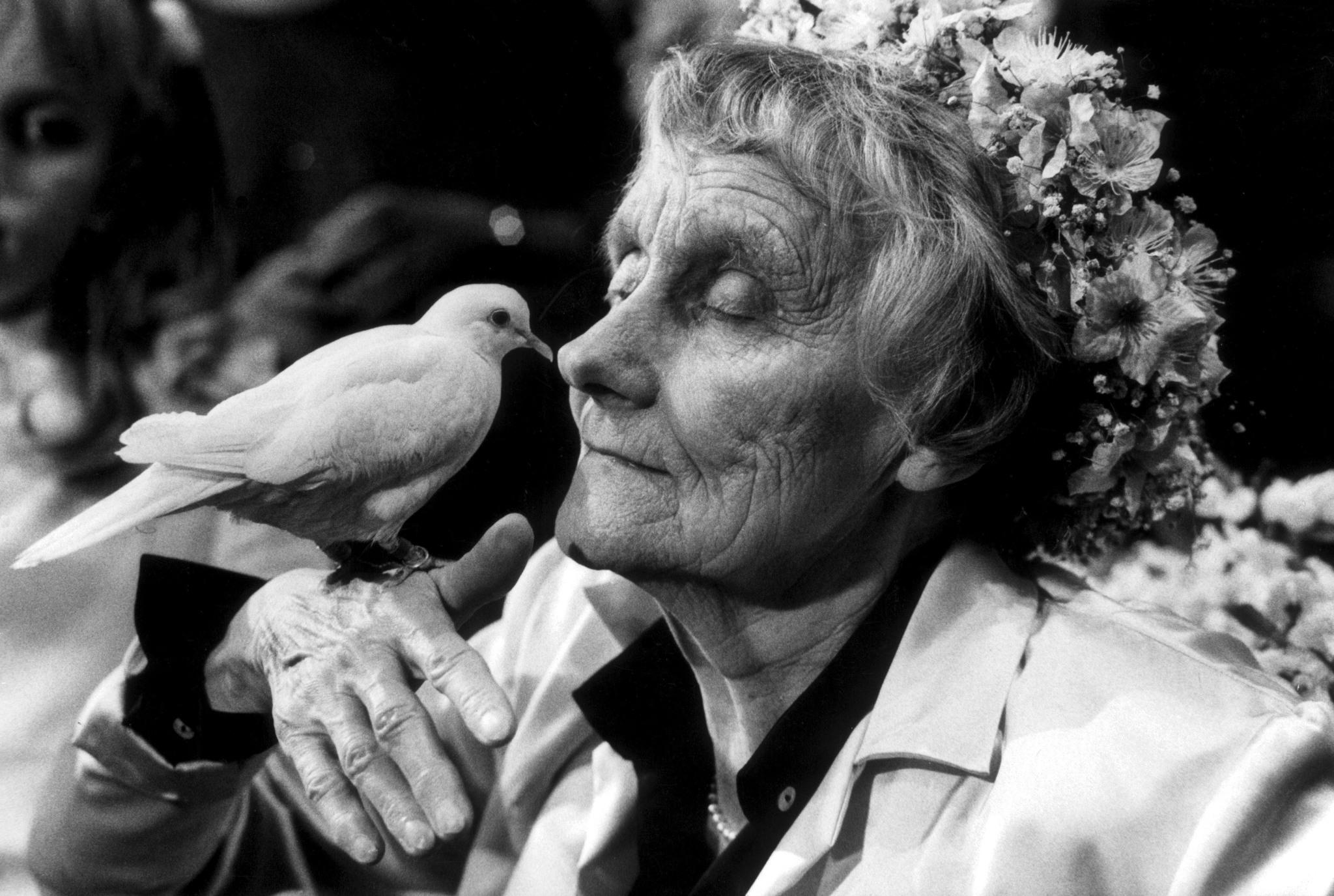 A black-and-white photo of Astrid Lindgren with a flower wreath on her head and a white dove on her hand.
