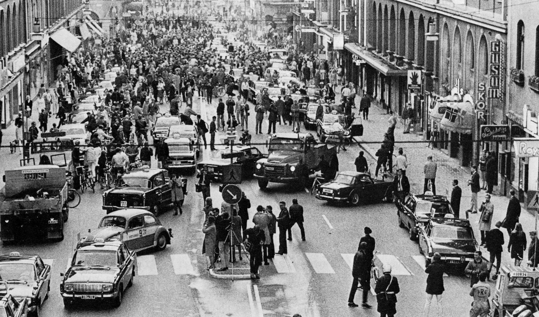 A black-and-white photo showing a city street full of cars going in different directions and pedestrians.