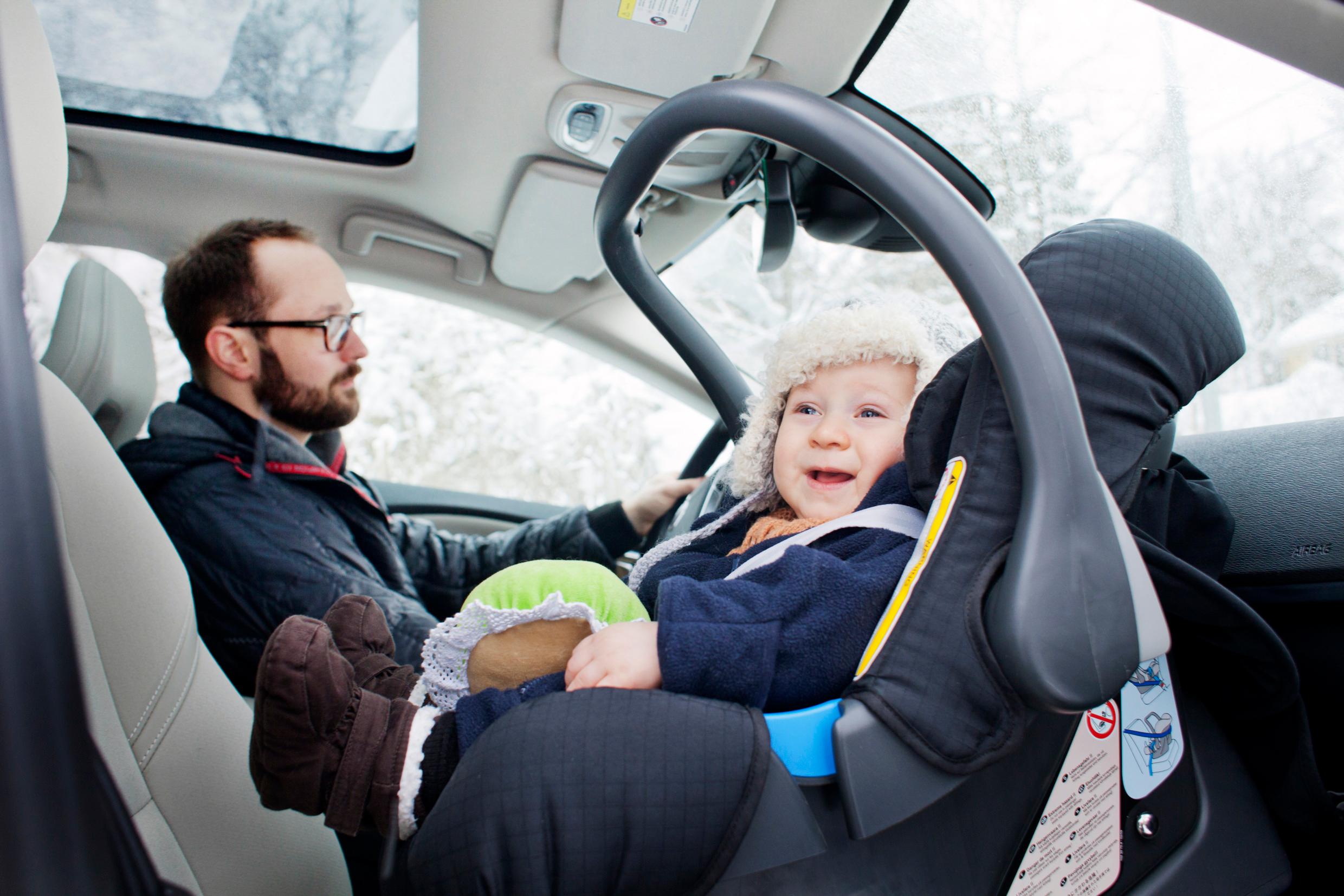 A baby in a baby car seat next to a man in the driver's seat.
