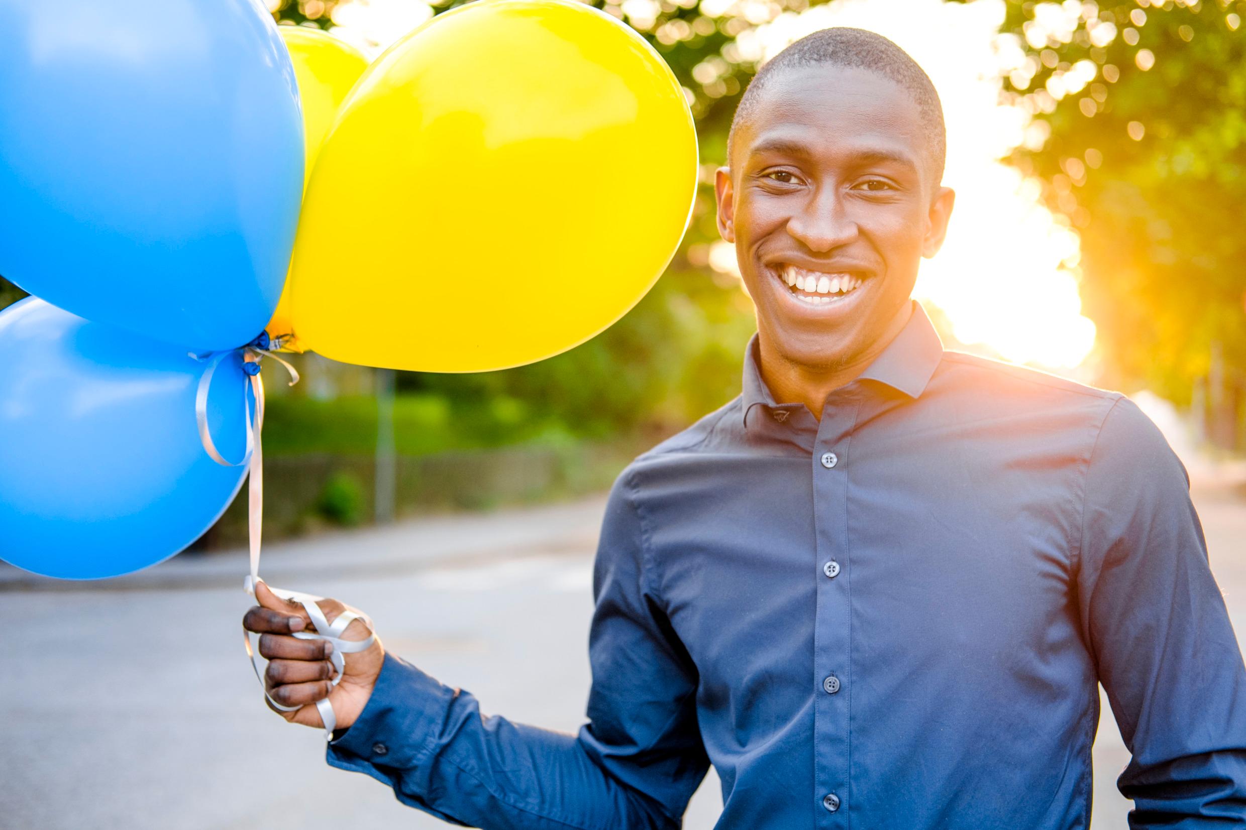 A man holding blue and yellow balloons in one hand.