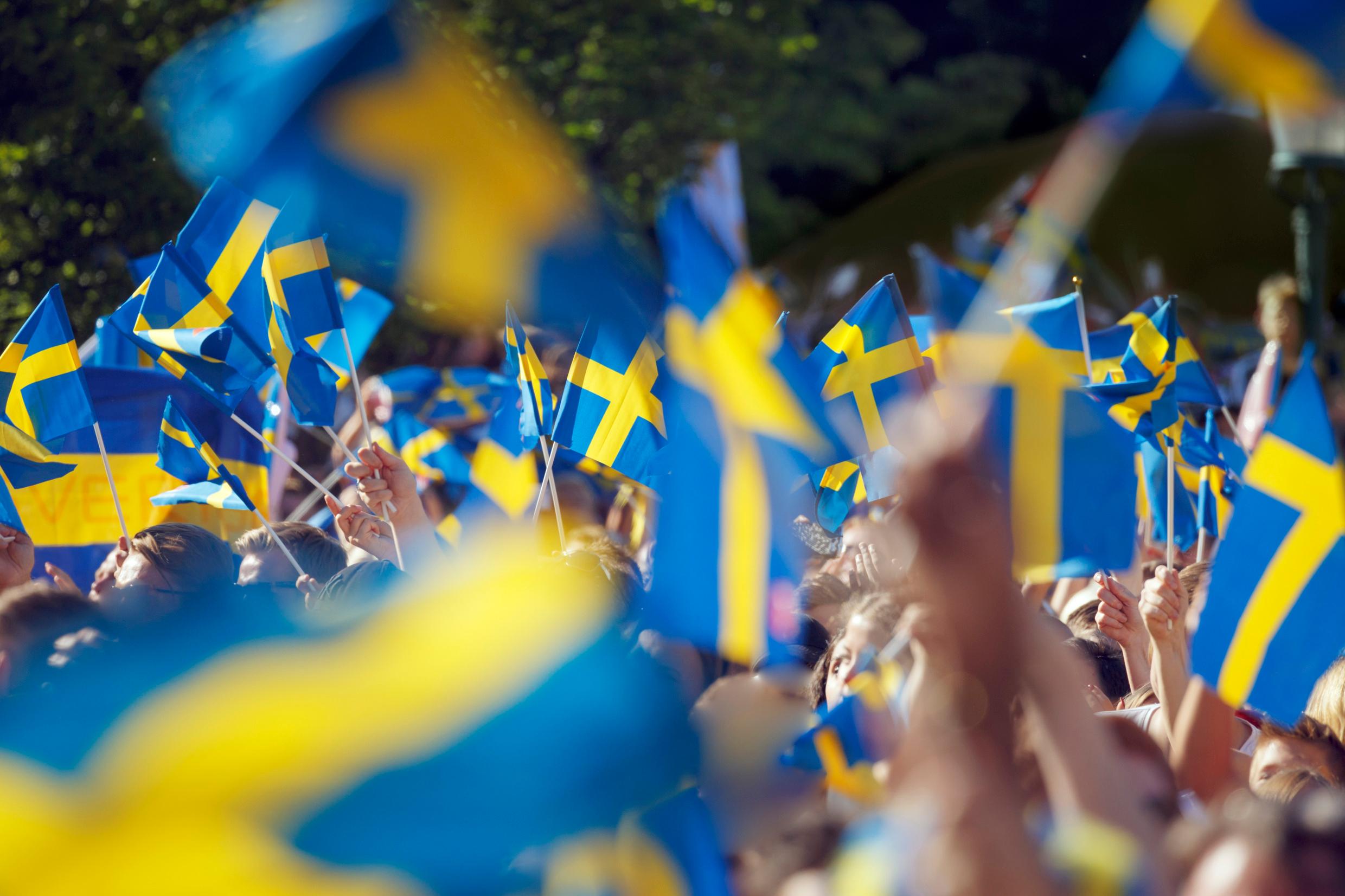 A big crowd waving numerous small Swedish flags in the air.