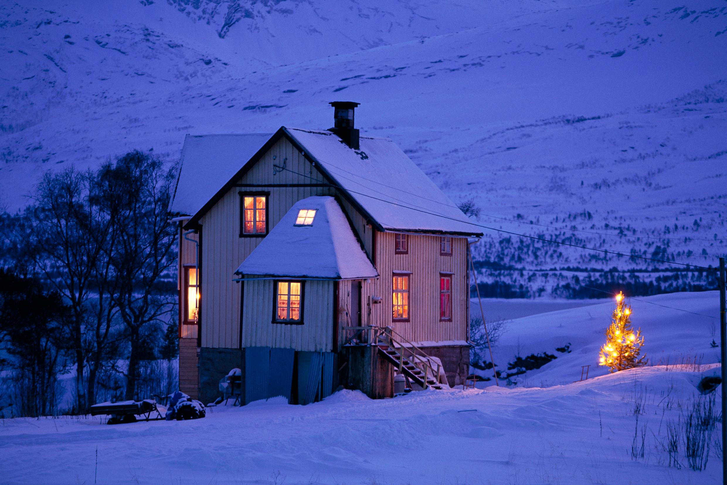 A countryside house warmly lit in the dark winter landscape.