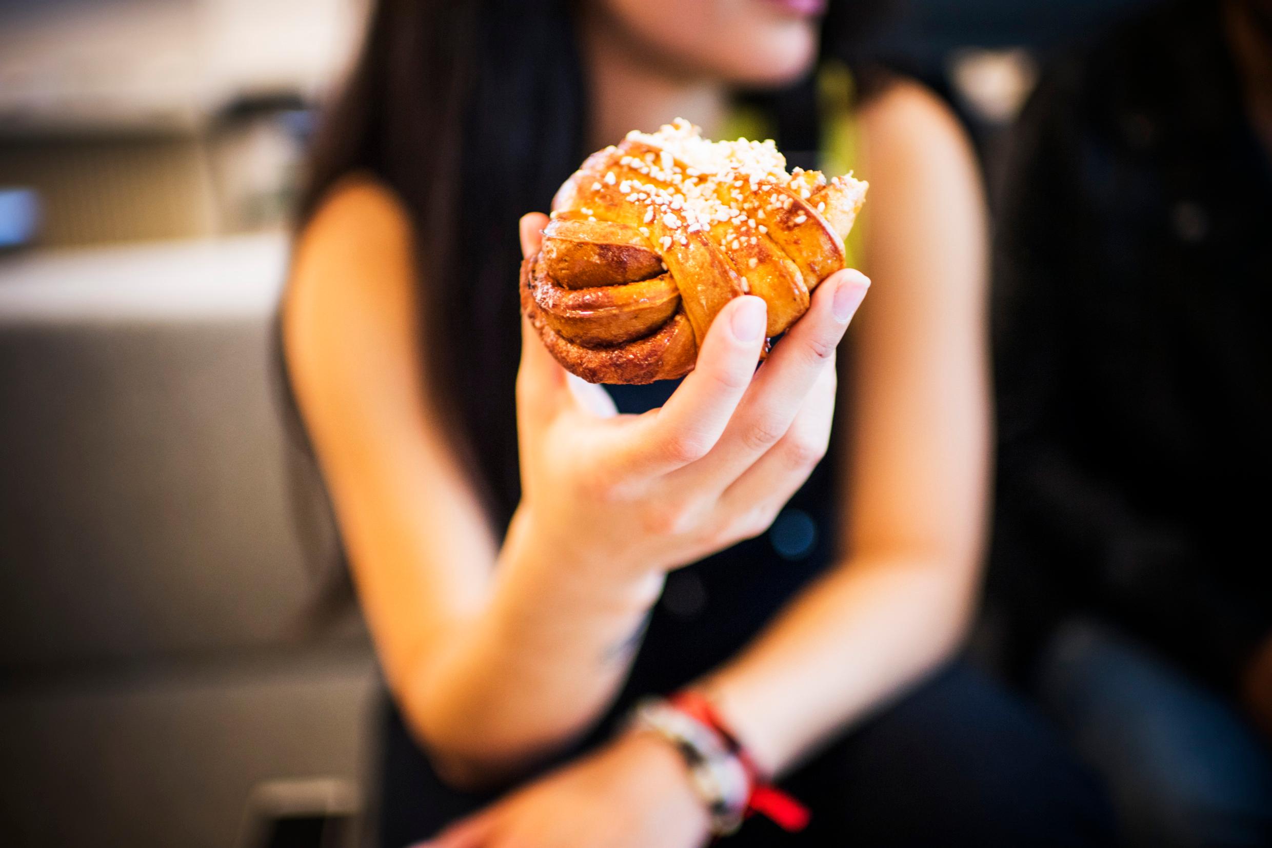 A person holding a cinnamon bun in an outstretched arm.