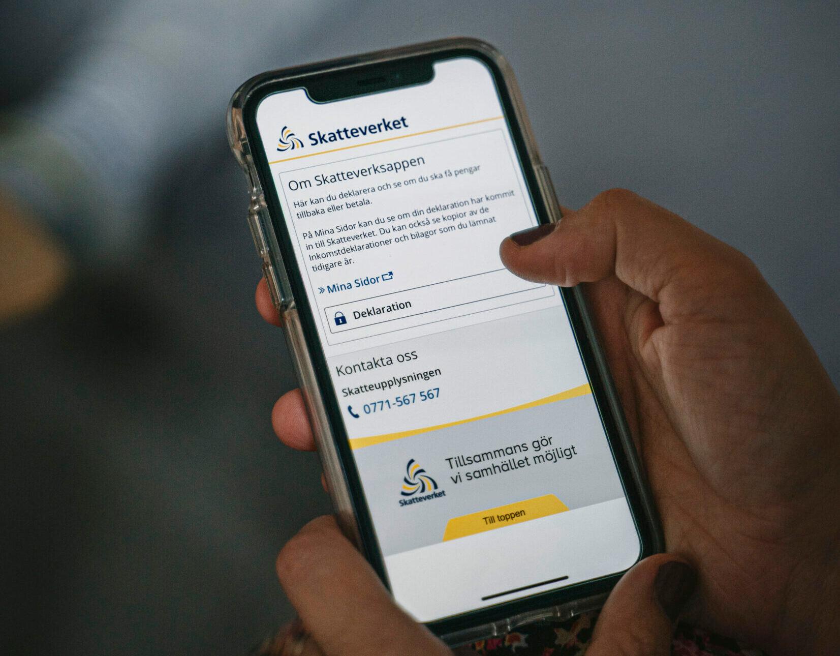 A hand holding a mobile phone with the Swedish Tax Agency's app on the screen.