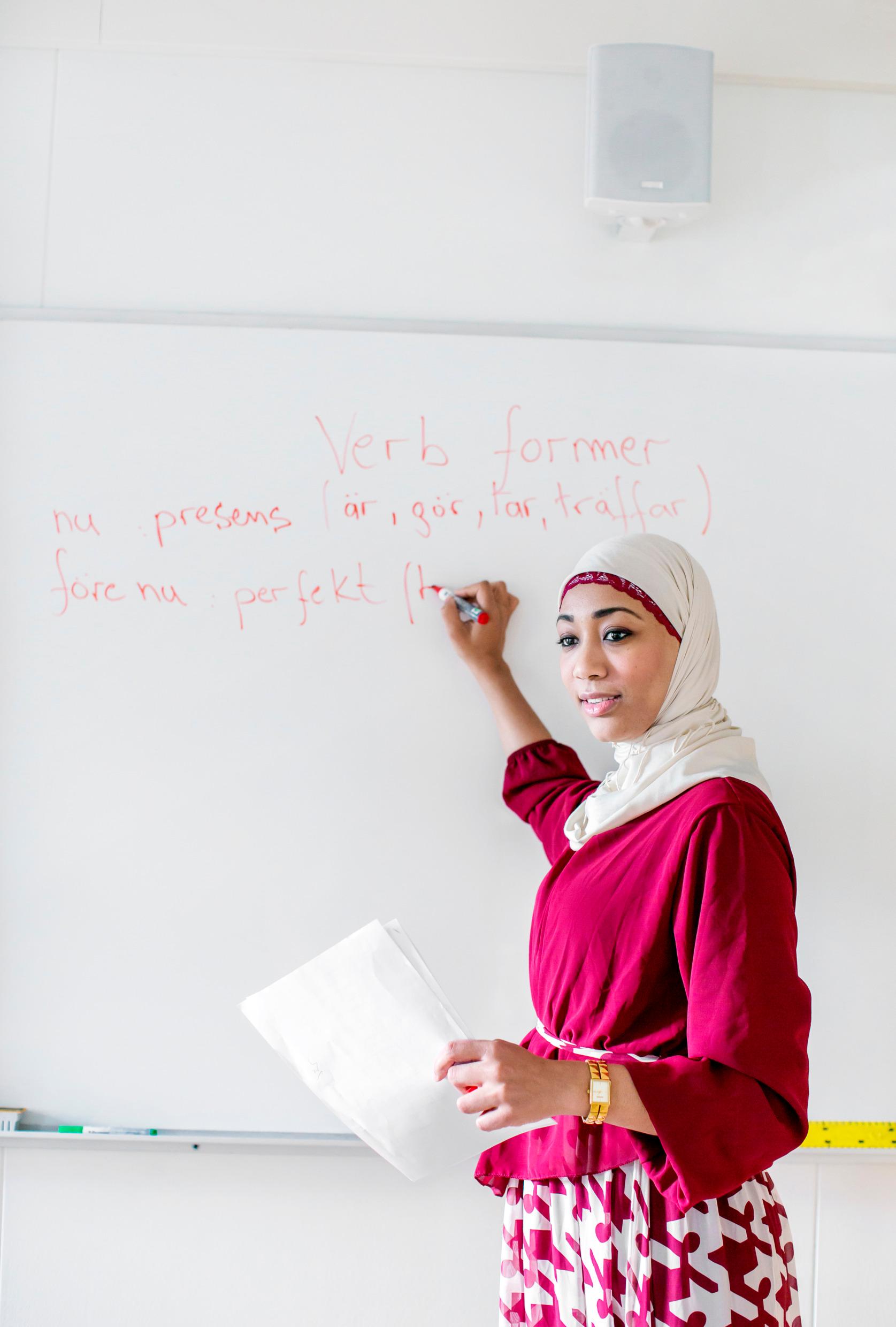 A woman standing by a whiteboard, writing words in Swedish.