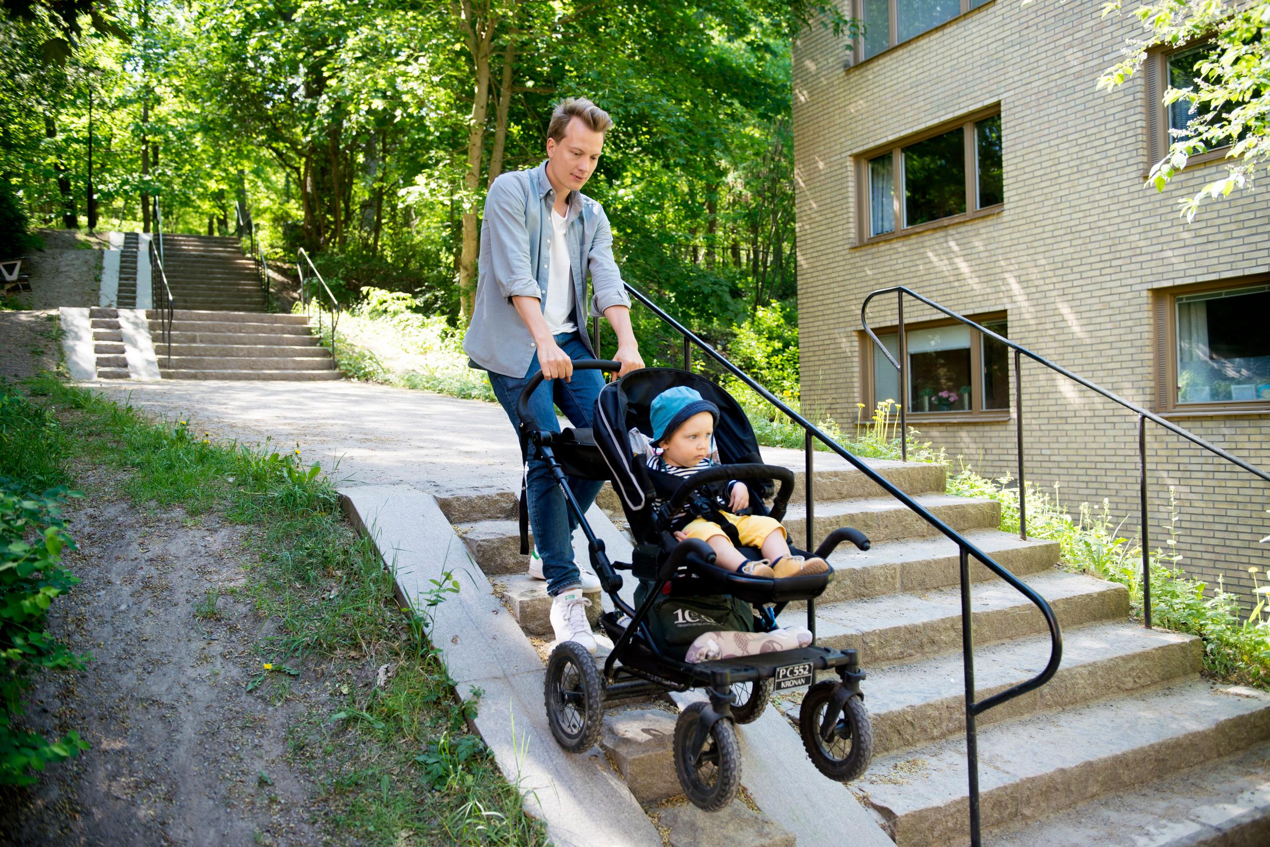 A man pushes a baby stroller down a ramp next to some steps.