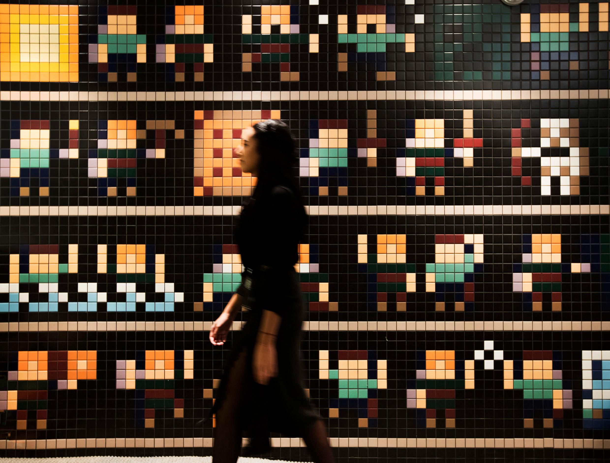 A woman walking past a wall of mosaic with figures resembling Minecraft characters.