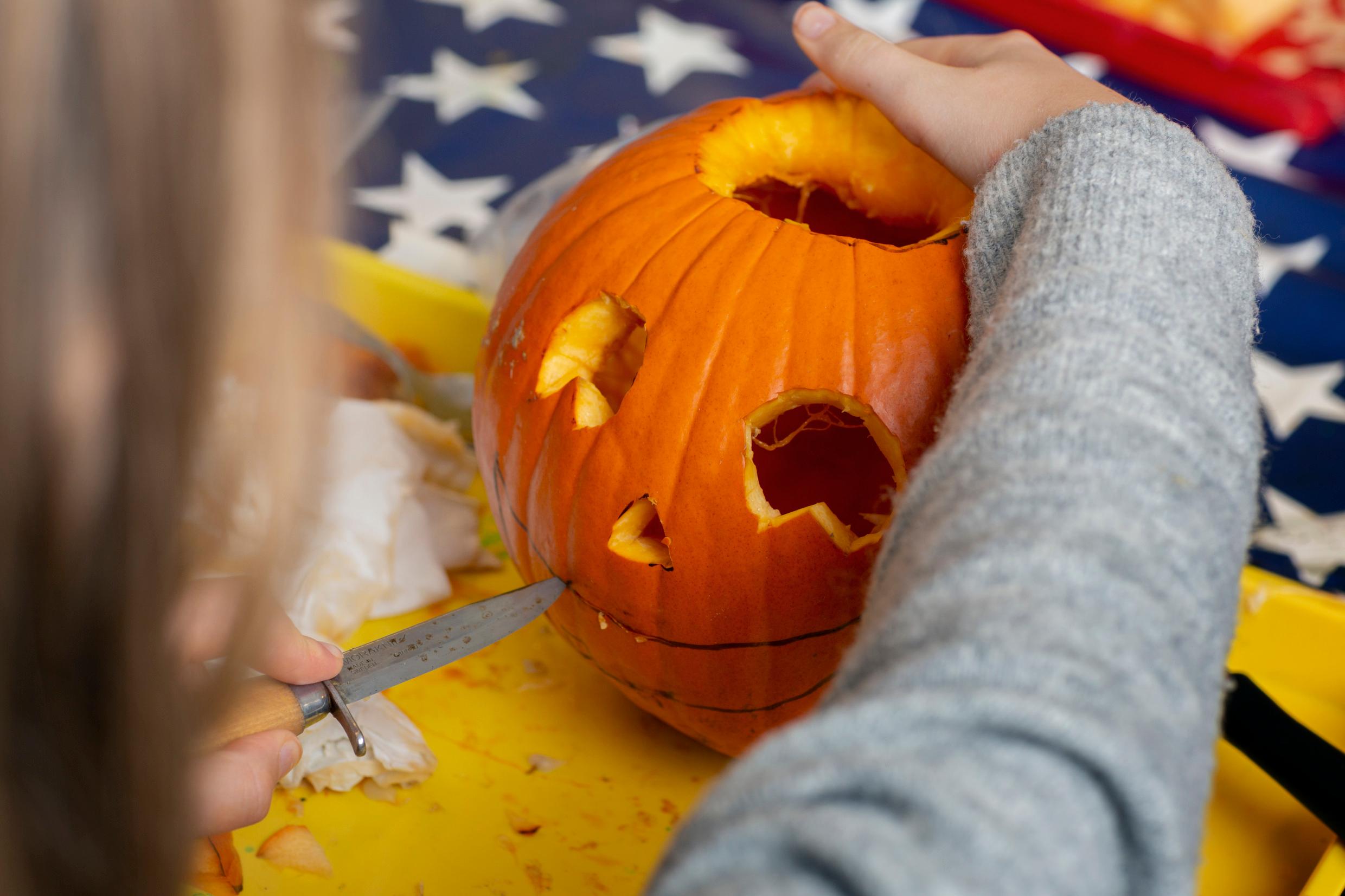 The hand of a child carving a Halloween pumpkin.
