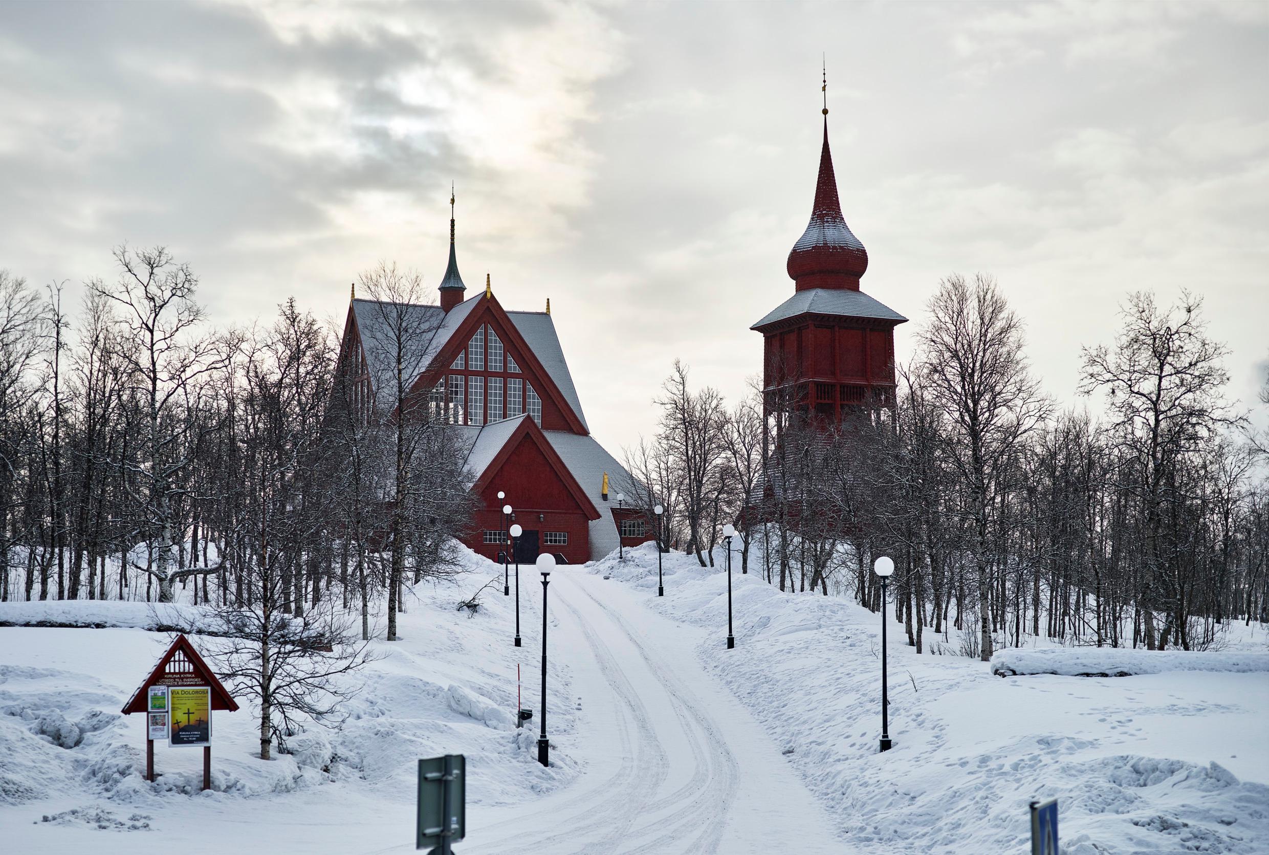 The Kiruna Church, a wooden building with a separate bell tower, sits on a snow-clad slope.